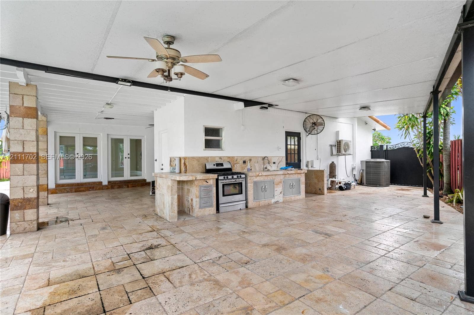 Covered patio featuring stone-tile flooring, outdoor kitchen with a built-in range and sink, ceiling fans, and structural stone pillars