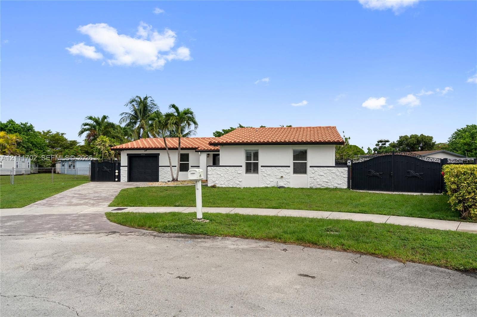 Single-story exterior featuring a textured masonry facade, terracotta-style roof tiles, an attached garage, and custom black metal perimeter gates