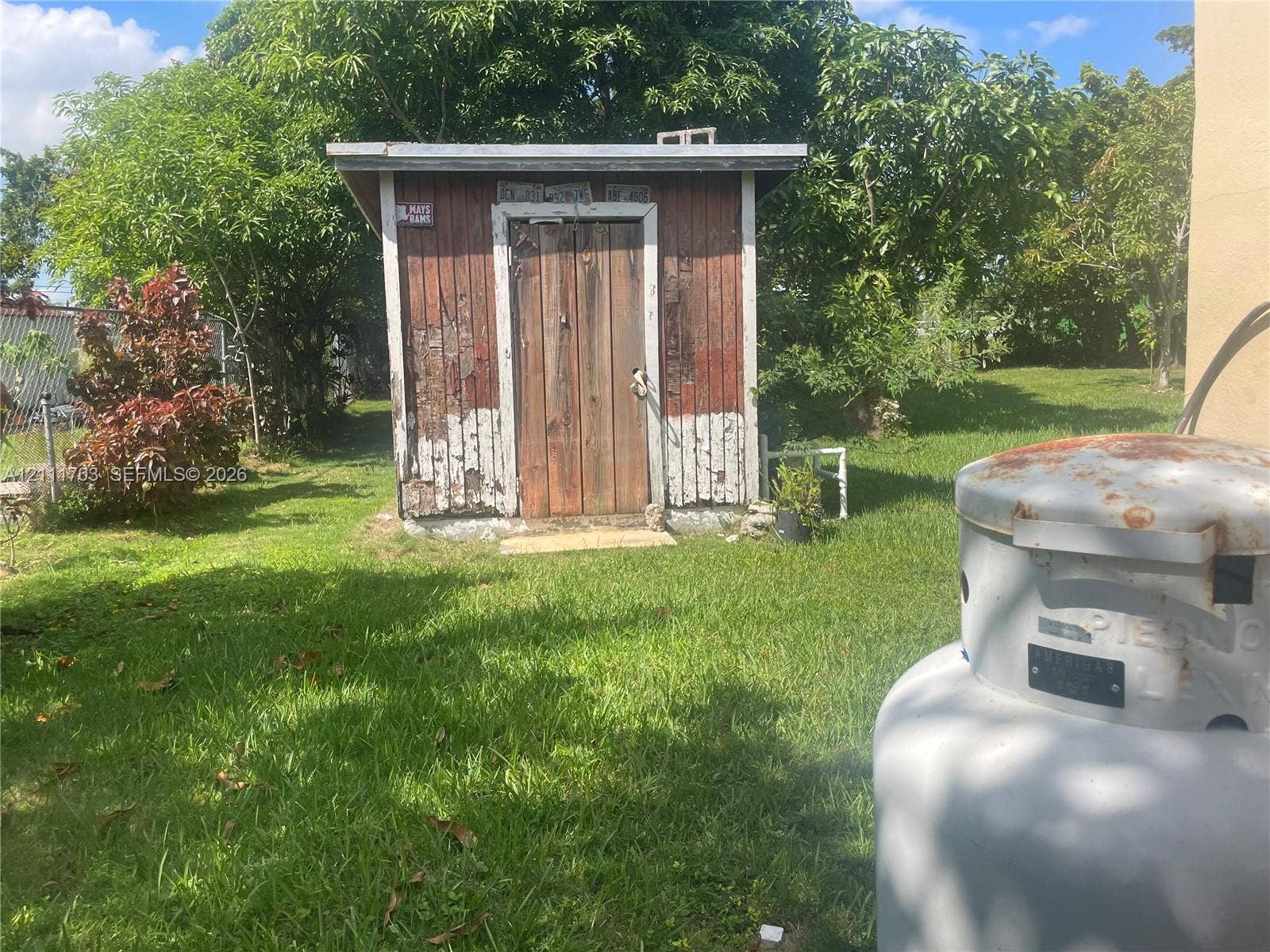 21840 SW 118th Avenue, Miami, FL 33170 Outdoor storage shed with wood-paneled exterior and single door, situated on a grass-covered lot with mature trees