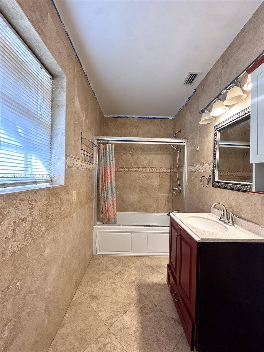 2222 SW 19th Avenue, Miami, Miami, FL 33145 Full-height stone wall tiling with decorative inlay, walk-in bathtub with sliding glass doors, dark wood-finish vanity, light-toned stone countertop with an integrated sink, and wall-mounted vanity lighting