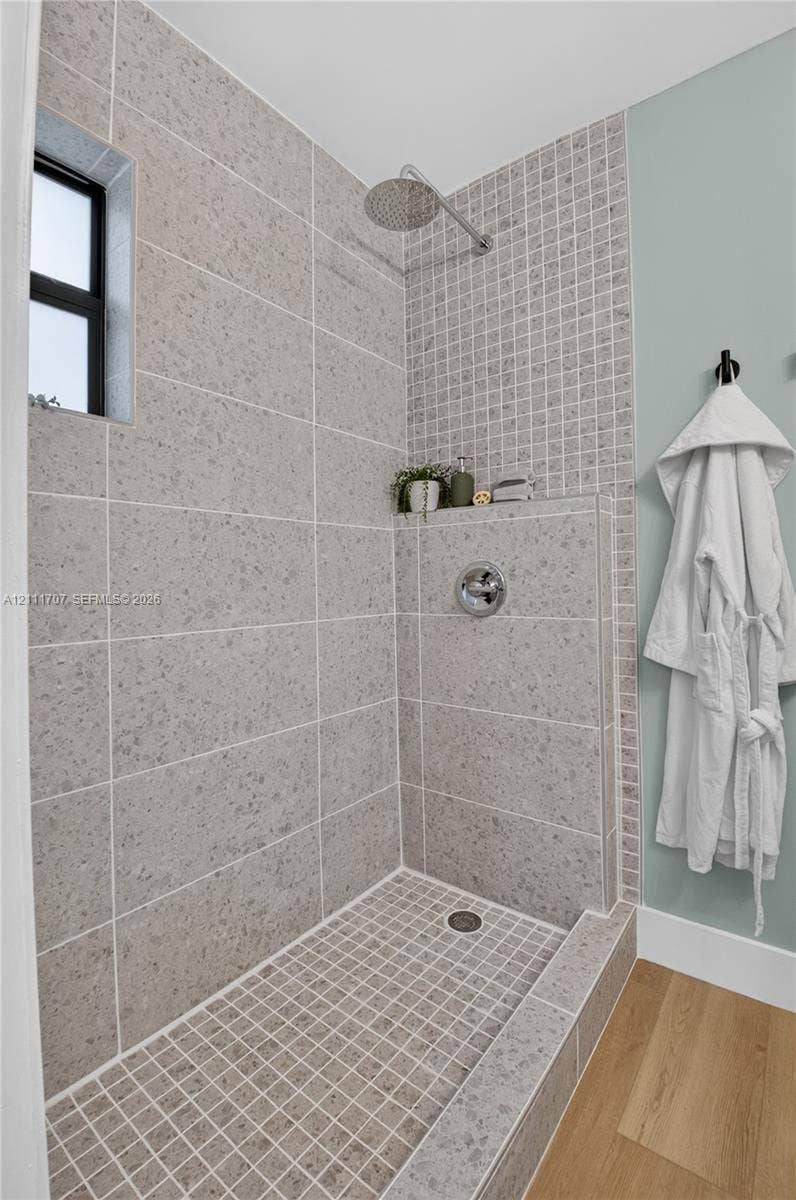 301 SW 12th Avenue, Delray Beach, FL 33444 Walk-in shower featuring large-format neutral tile walls, a mosaic tile shower floor and accent wall, a built-in recessed shelf, a wall-mounted rainfall showerhead, and wood-finish flooring