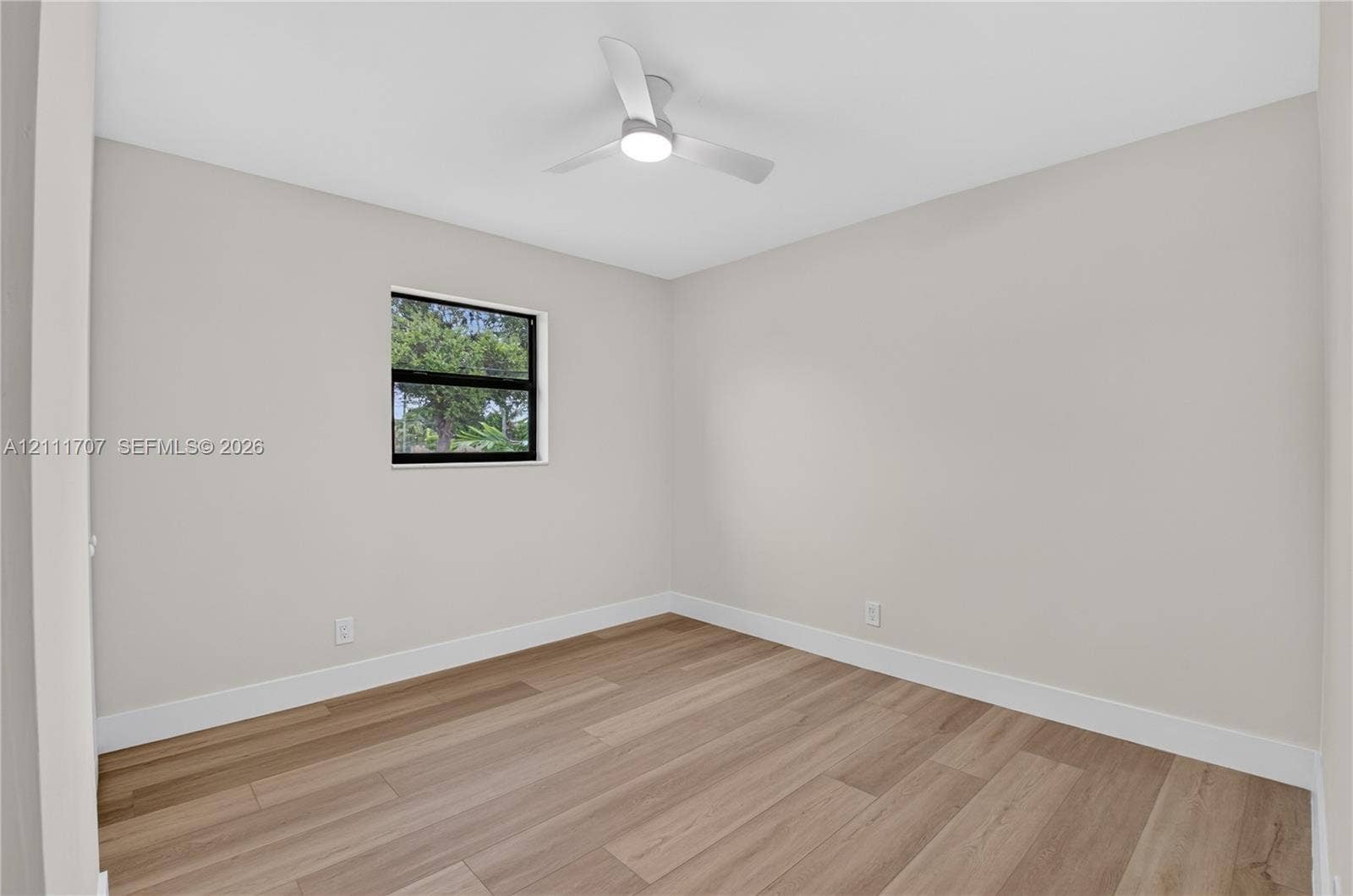 301 SW 12th Avenue, Delray Beach, FL 33444 Neutral-toned walls, wood-finish flooring, and a modern ceiling fan with integrated lighting, featuring a single window with black framing