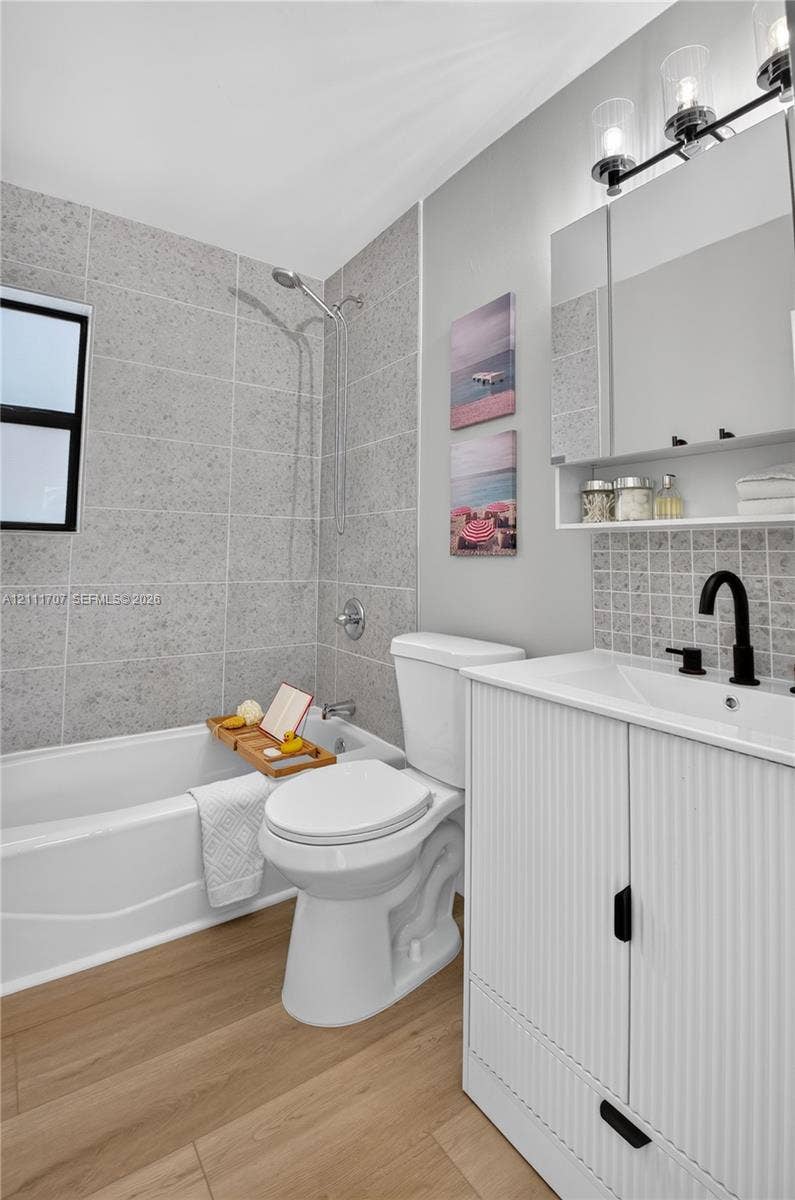301 SW 12th Avenue, Delray Beach, FL 33444 Bathroom featuring a ribbed-detail vanity with a matte black faucet, wood-finish flooring, a tub-shower combination with full-height stone-look tile surround, and a tri-light vanity fixture