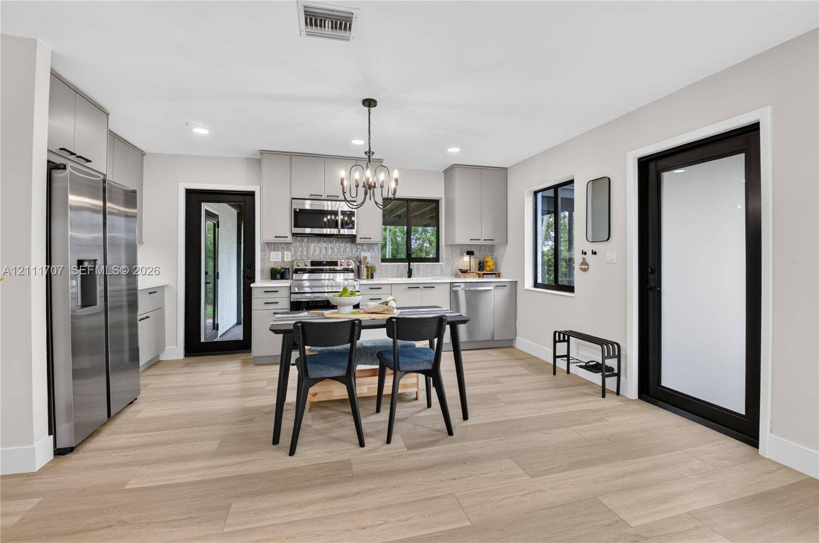 301 SW 12th Avenue, Delray Beach, FL 33444 Kitchen featuring light-toned beige cabinetry, stainless steel appliances, wood-finish flooring, two exterior doors with black frames, and a multi-light chandelier