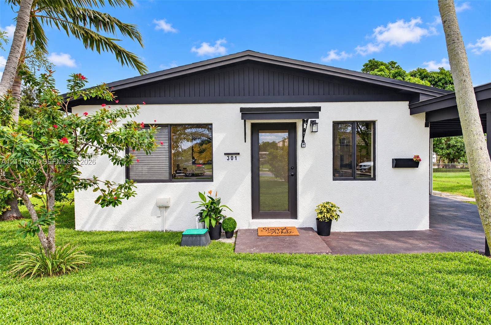 301 SW 12th Avenue, Delray Beach, FL 33444 Stucco exterior featuring vertical board-and-batten siding, dark-trimmed windows, a glass-panel entry door, and an attached carport