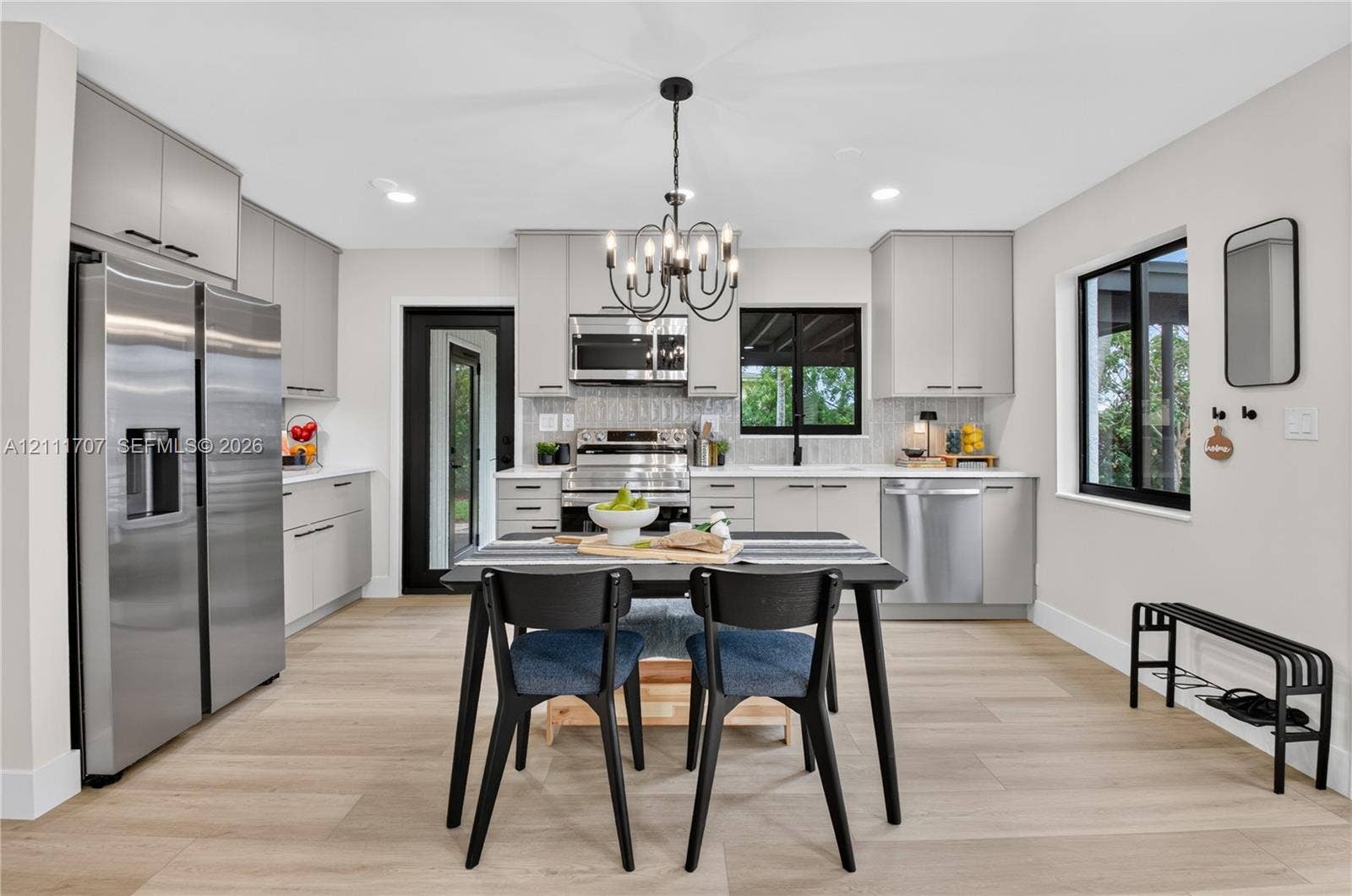 301 SW 12th Avenue, Delray Beach, FL 33444 Kitchen featuring light beige cabinetry, stainless steel appliances, wood-finish flooring, a multi-arm chandelier, and a black-framed exterior door