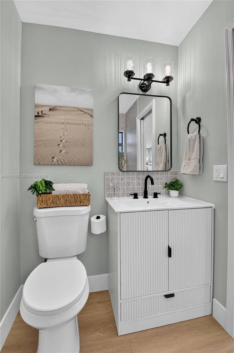 301 SW 12th Avenue, Delray Beach, FL 33444 Modern vanity featuring a fluted cabinet design, rectangular white countertop, and matte black hardware, accompanied by a three-light fixture, framed mirror, and wood-finish flooring