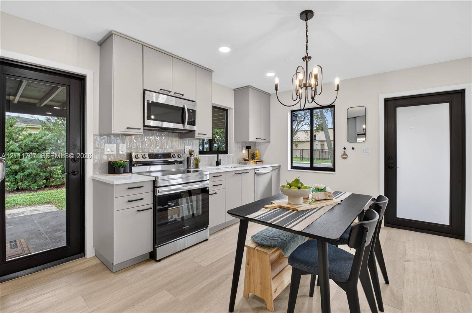 301 SW 12th Avenue, Delray Beach, FL 33444 Kitchen featuring beige flat-panel cabinetry, stainless steel appliances, a textured tile backsplash, wood-finish flooring, and a multi-light chandelier