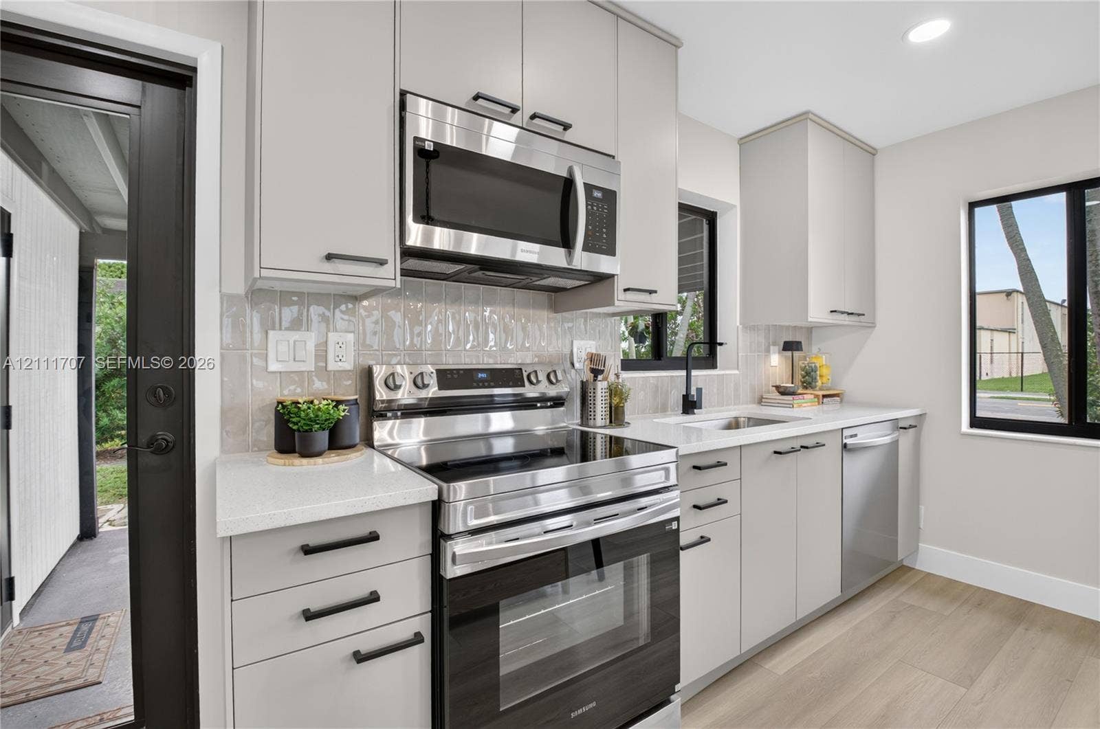 301 SW 12th Avenue, Delray Beach, FL 33444 Kitchen featuring flat-panel beige cabinetry, stone-finish countertops, stainless steel appliances, a textured tile backsplash, and wood-finish flooring