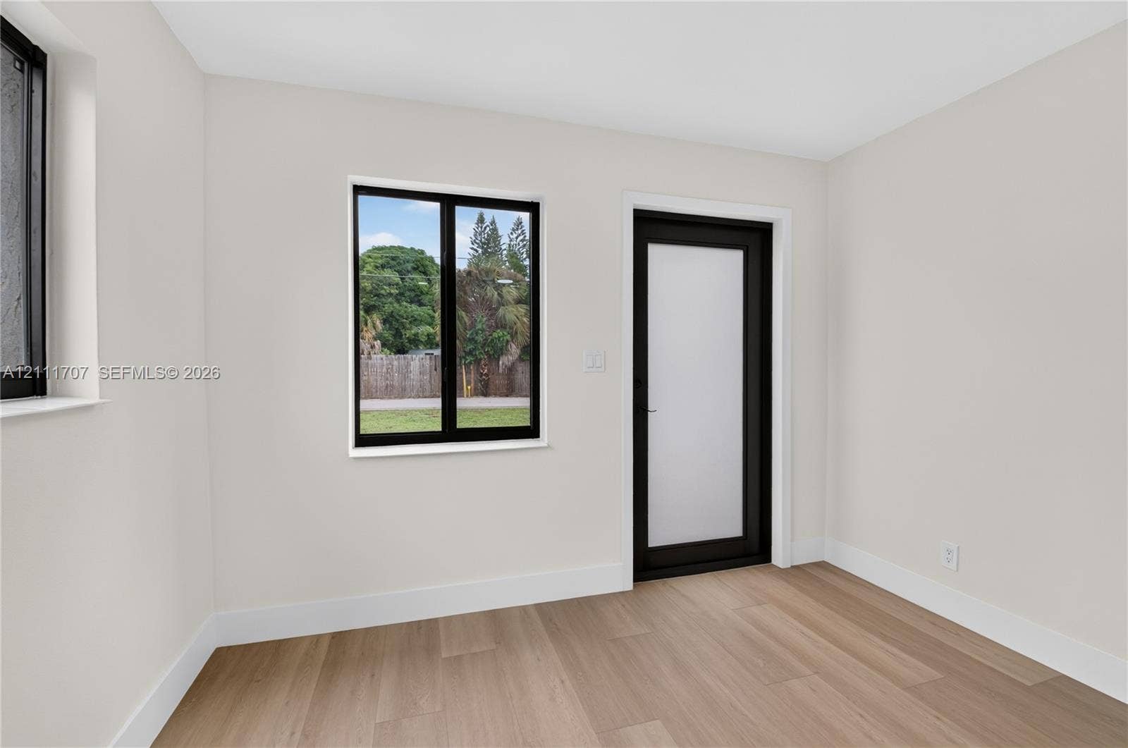 301 SW 12th Avenue, Delray Beach, FL 33444 Interior space featuring neutral-toned walls, wood-finish flooring, black-framed windows, and a black-framed door with a frosted glass panel