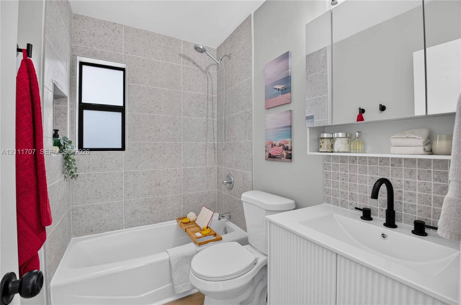 301 SW 12th Avenue, Delray Beach, FL 33444 Bathroom featuring a white vanity with a rectangular sink, matte black fixtures, full-width mirrored medicine cabinet, a tiled shower surround with a built-in recessed niche, and a neutral-toned tile backsplash