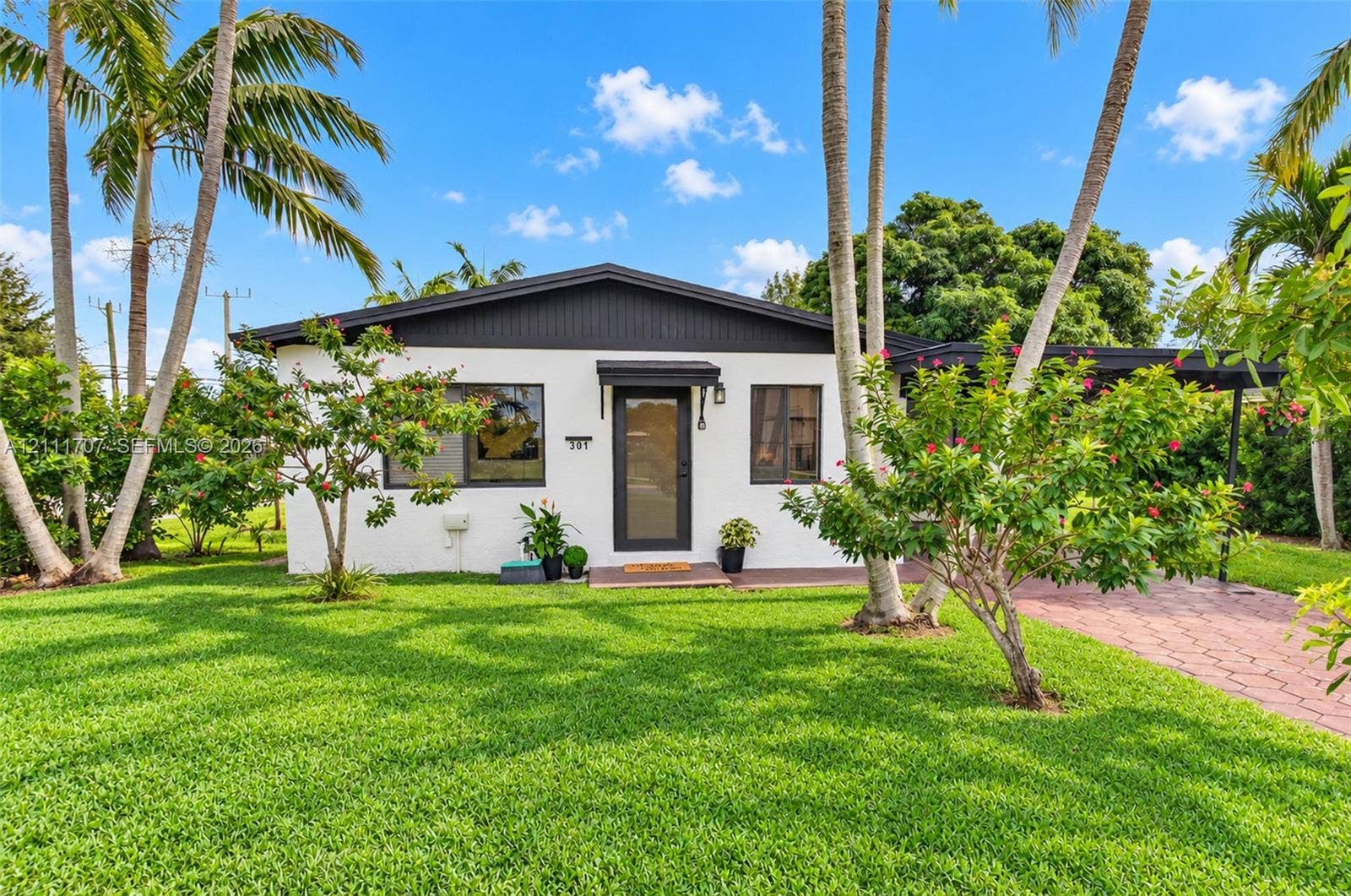 301 SW 12th Avenue, Delray Beach, FL 33444 Single-story exterior featuring white stucco siding, a dark-toned gable roof, a covered entryway, and a patterned paver driveway