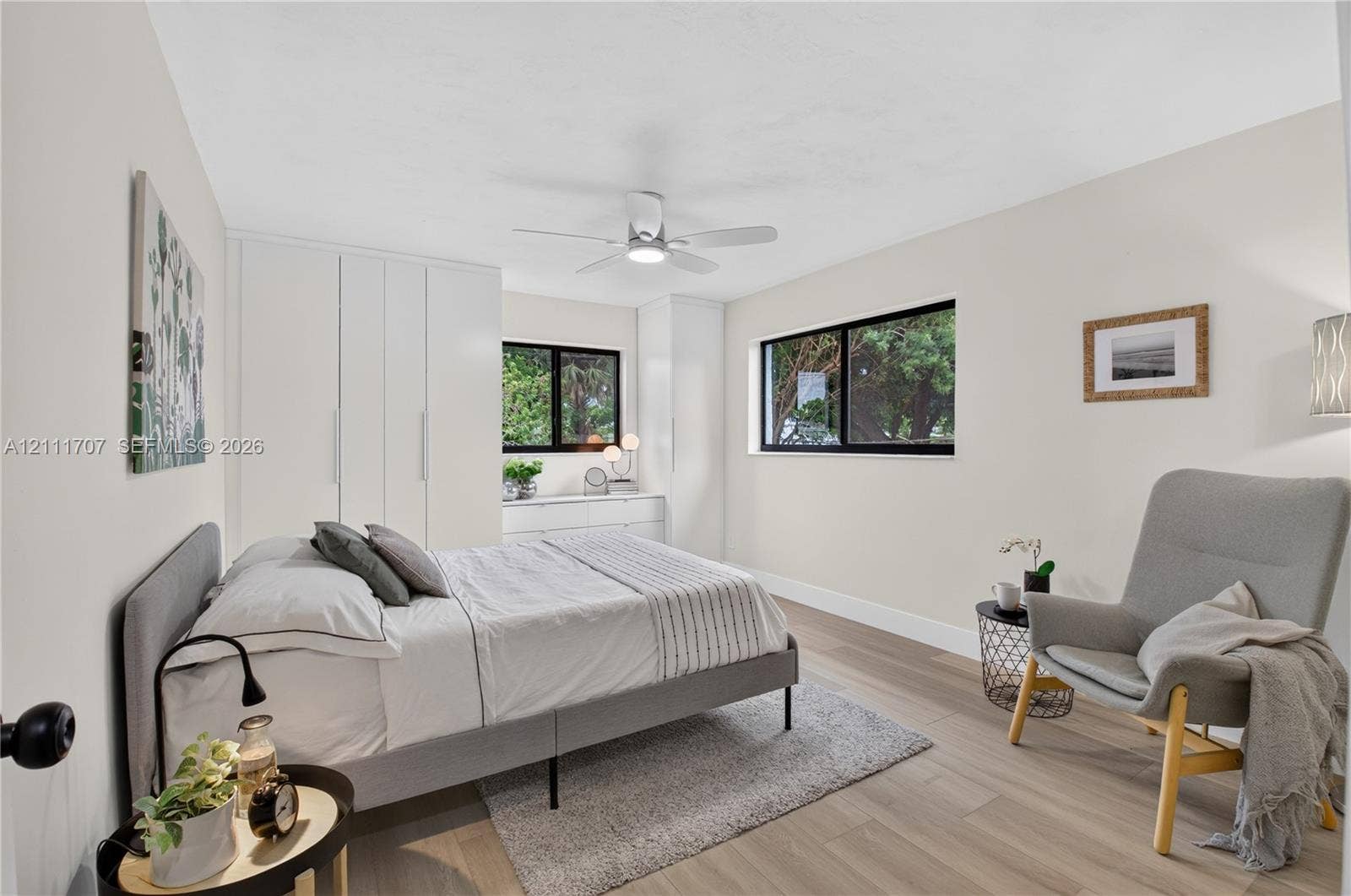 301 SW 12th Avenue, Delray Beach, FL 33444 Bedroom featuring wood-finish flooring, floor-to-ceiling built-in closet cabinetry, dual black-frame windows, and a ceiling-mounted light fixture with integrated fan