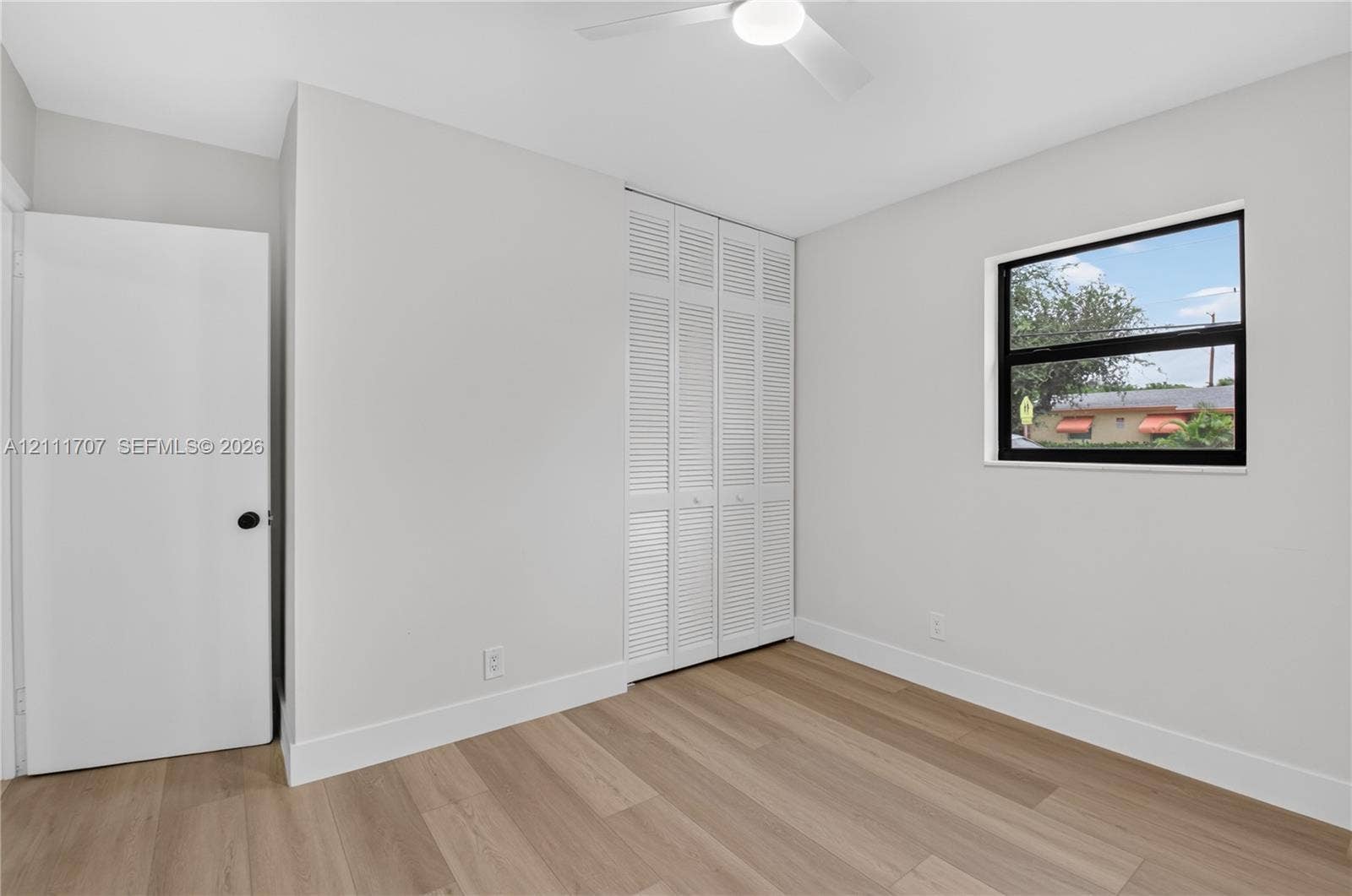 301 SW 12th Avenue, Delray Beach, FL 33444 Room featuring wood-finish flooring, white louvered closet doors, a ceiling fan, and a window with a black frame