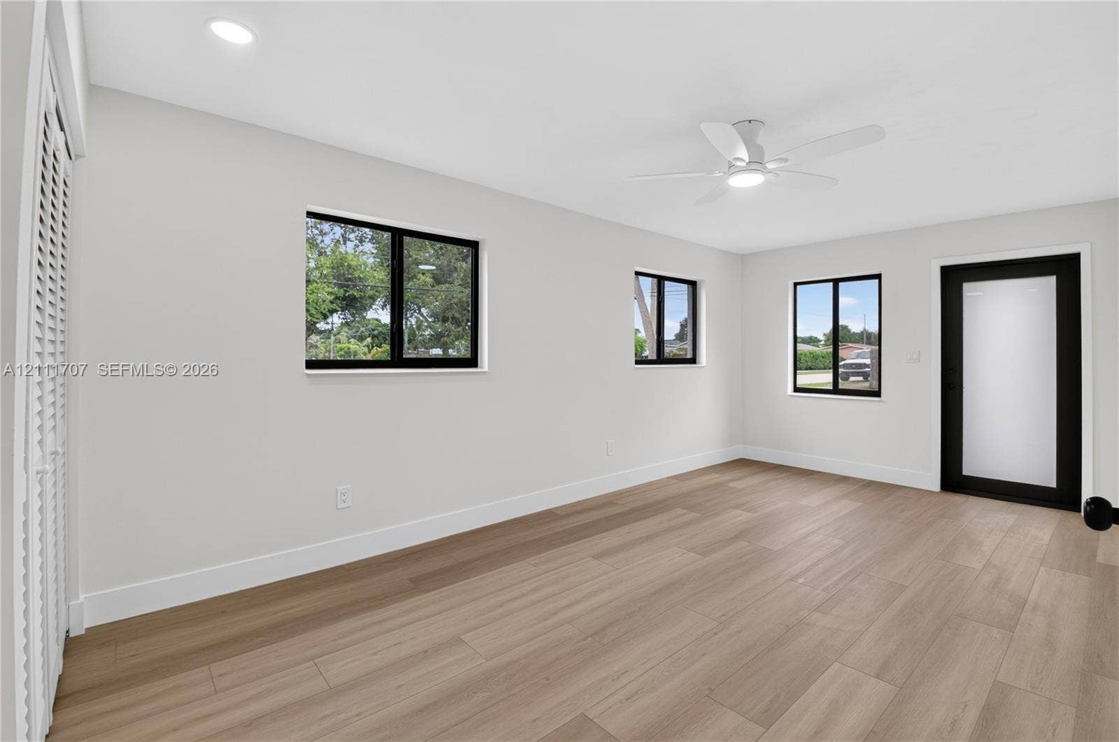 301 SW 12th Avenue, Delray Beach, FL 33444 Light-filled room featuring wood-finish flooring, recessed lighting, a modern ceiling fan, multiple windows with black framing, and a frosted glass exterior door