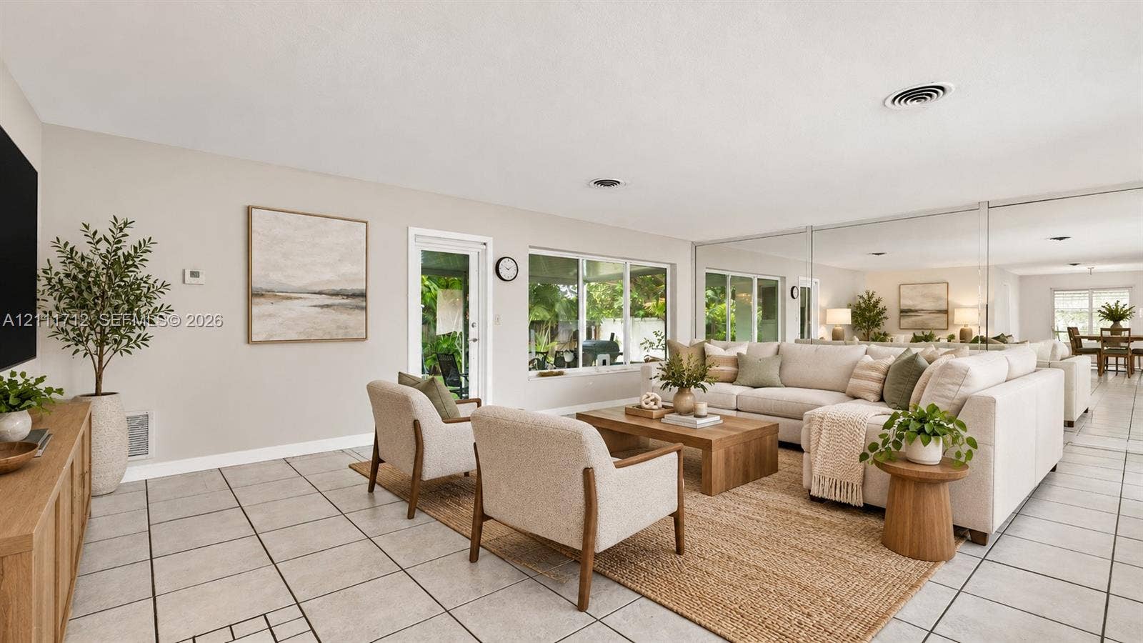 Virtually staged. Neutral-toned living space featuring oversized wall-to-wall mirrors, large format floor tiling, and a glass-paneled exterior door