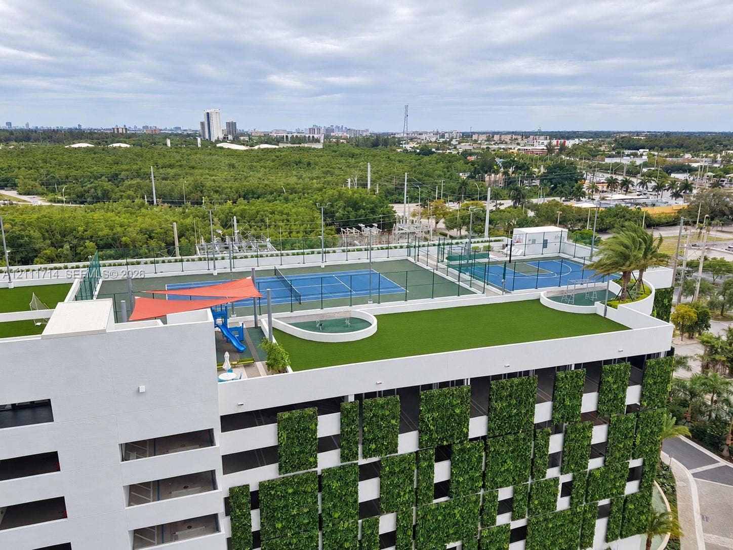 Rooftop amenities featuring multiple fenced sport courts, synthetic turf recreation areas, and a vertical green wall facade