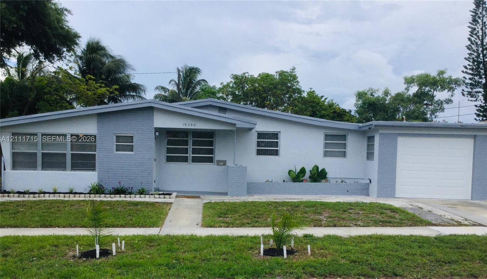 18280 NE Glades Drive, North Miami Beach, North Miami Beach, FL 33162 Single-story residence featuring a painted brick facade, a low-pitch roofline, horizontal multi-pane windows, and an attached one-car garage