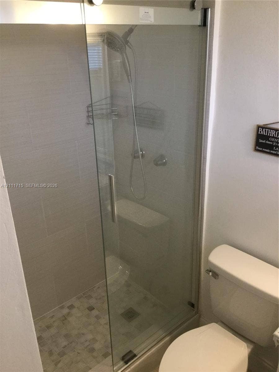 18280 NE Glades Drive, North Miami Beach, North Miami Beach, FL 33162 Walk-in shower enclosure featuring a sliding glass door, tiled walls, mosaic-tiled flooring, and a hand-held shower fixture