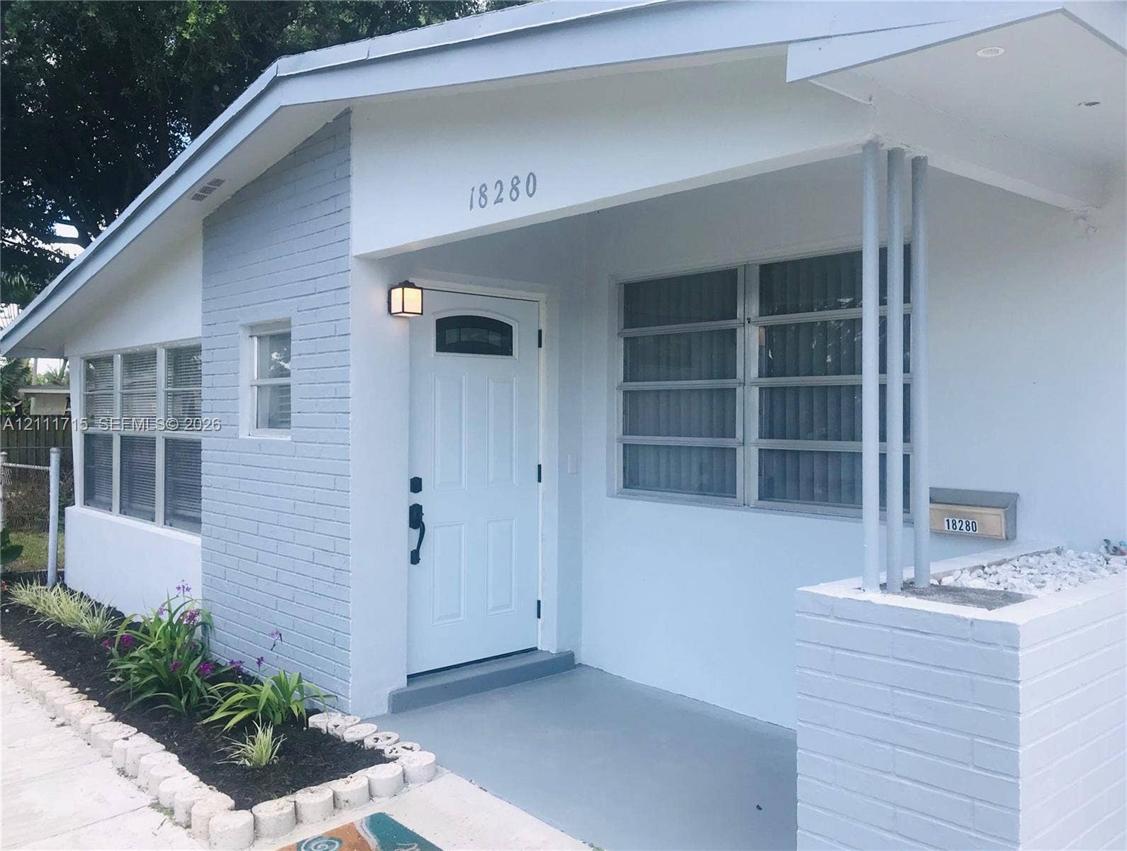 18280 NE Glades Drive, North Miami Beach, North Miami Beach, FL 33162 Exterior entrance featuring a painted brick facade, covered porch, multi-pane windows, and a built-in brick planter