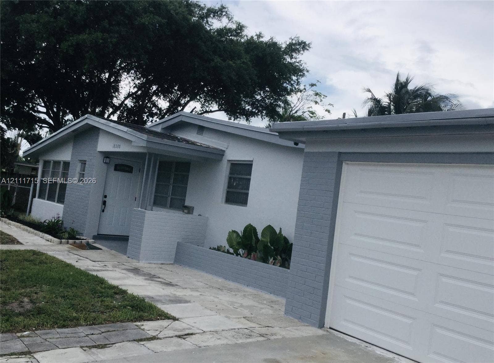 18280 NE Glades Drive, North Miami Beach, North Miami Beach, FL 33162 Single-story residence featuring a painted brick exterior, a covered entryway, an attached garage, and multi-pane windows
