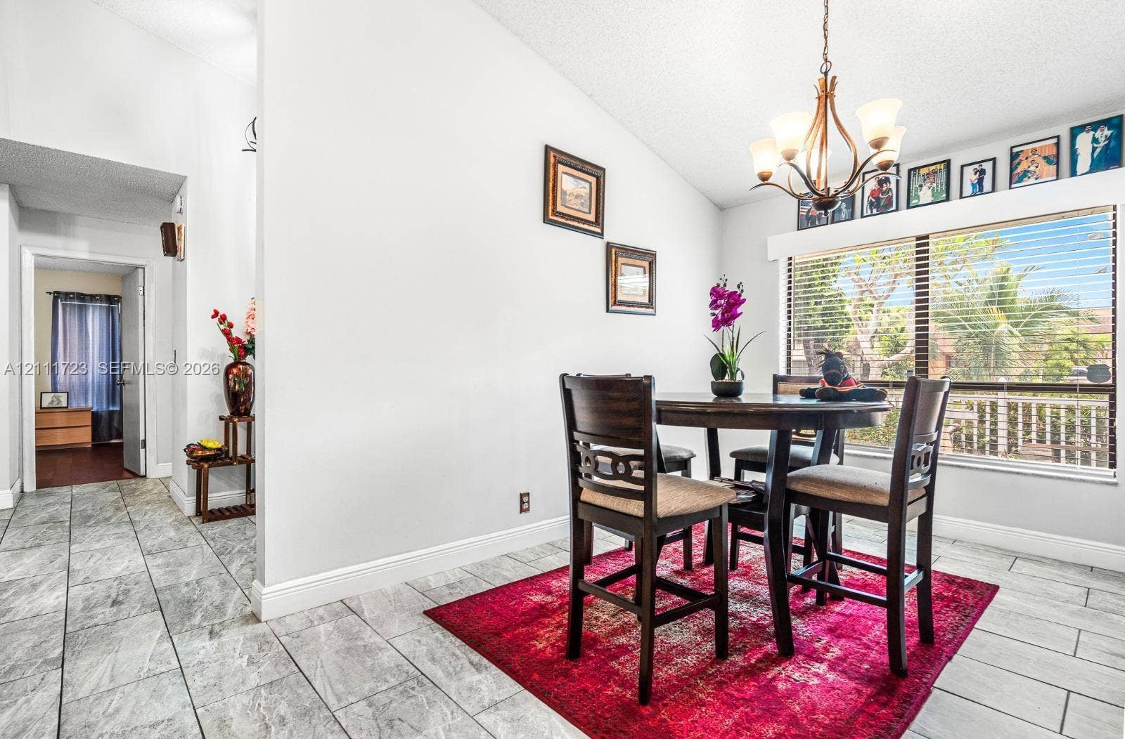 8541 NW 51st Court, Lauderhill, FL 33351 Vaulted ceilings, large window with horizontal blinds, and tile flooring featuring stone-finish detailing, illuminated by a multi-arm chandelier