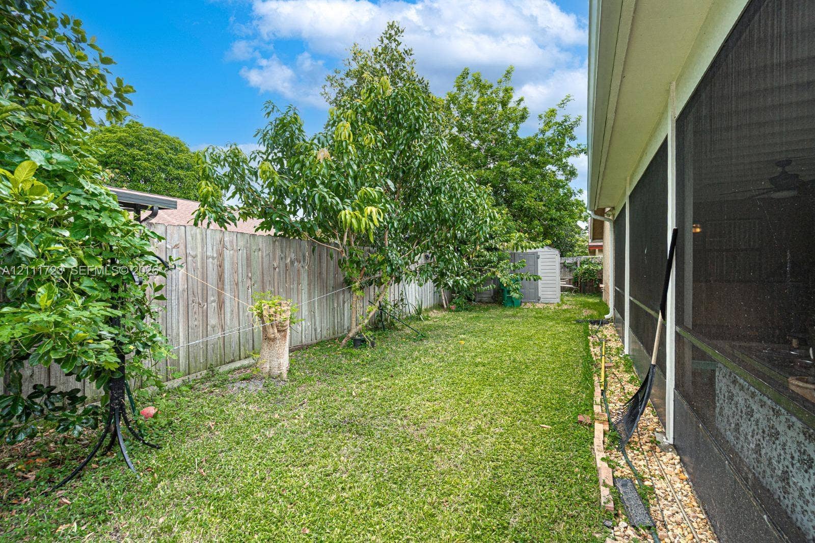 8541 NW 51st Court, Lauderhill, FL 33351 Rear yard featuring a grass lawn, mature trees, wood privacy fencing, and a screened enclosure