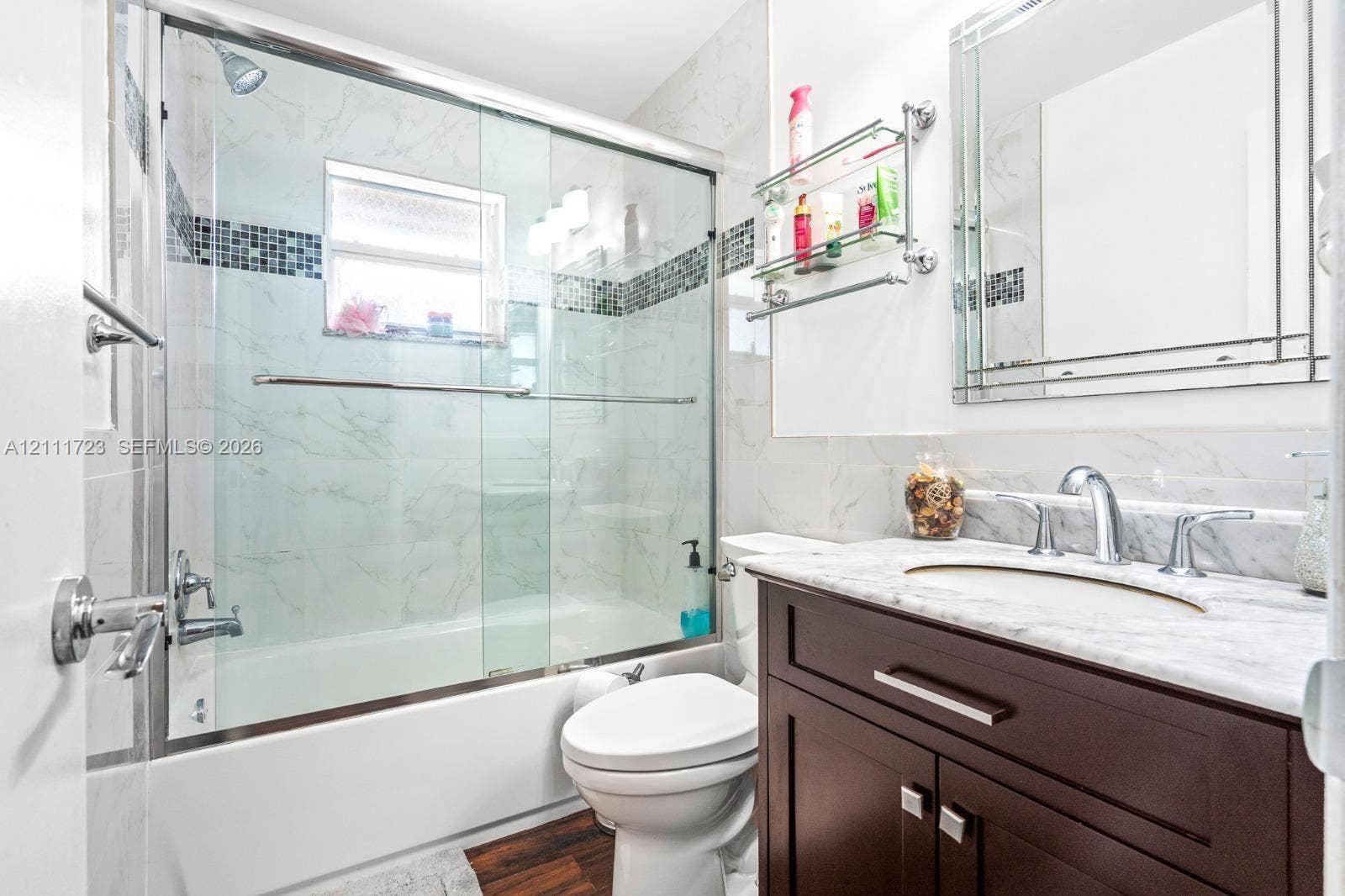 8541 NW 51st Court, Lauderhill, FL 33351 Bathroom featuring a dark wood-finish vanity with a stone countertop, an integrated undermount sink, a framed wall mirror, and a tiled tub shower combination with a glass sliding door
