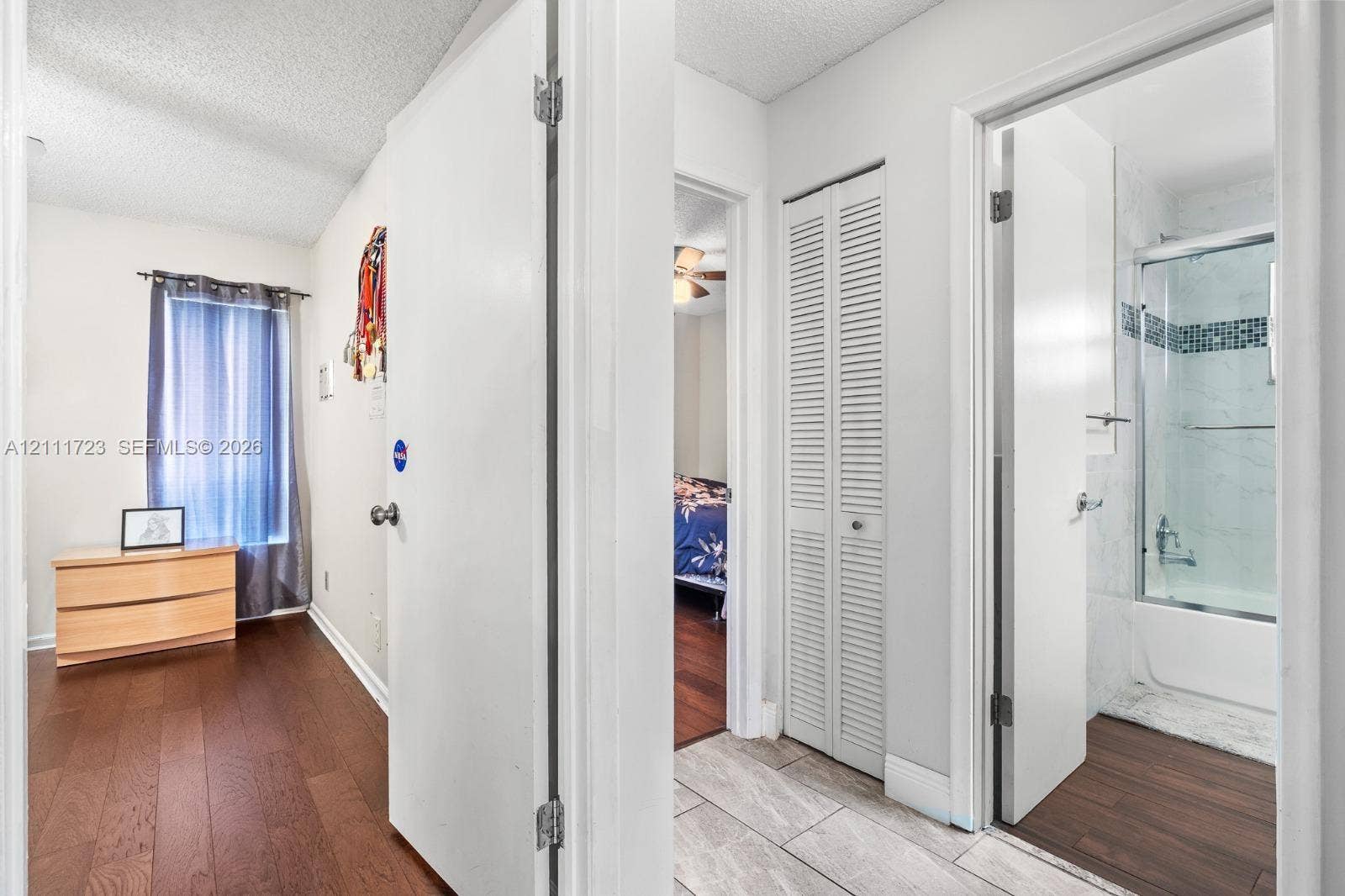8541 NW 51st Court, Lauderhill, FL 33351 Hallway featuring wood-finish flooring, white louvered closet doors, and tile flooring with access to a bathroom containing a shower-tub combination with tiled surround