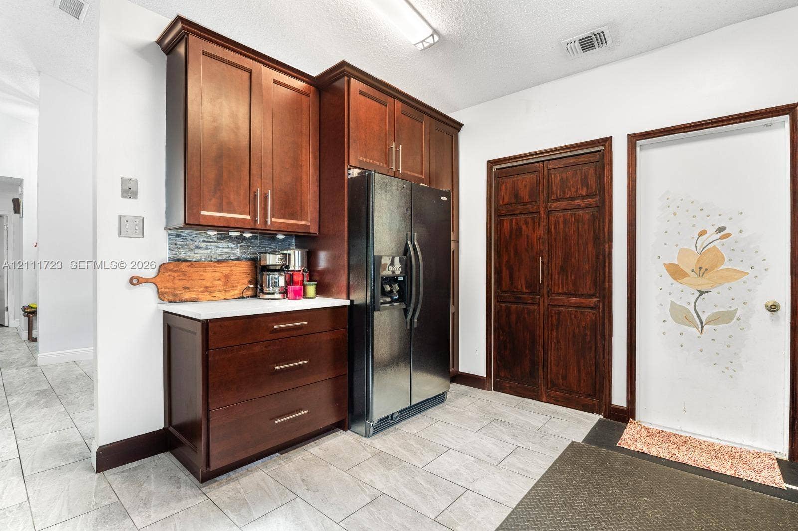 8541 NW 51st Court, Lauderhill, FL 33351 Rich-toned wood cabinetry with bar-style hardware, stainless steel refrigerator, tiled backsplash, and stone-finish flooring
