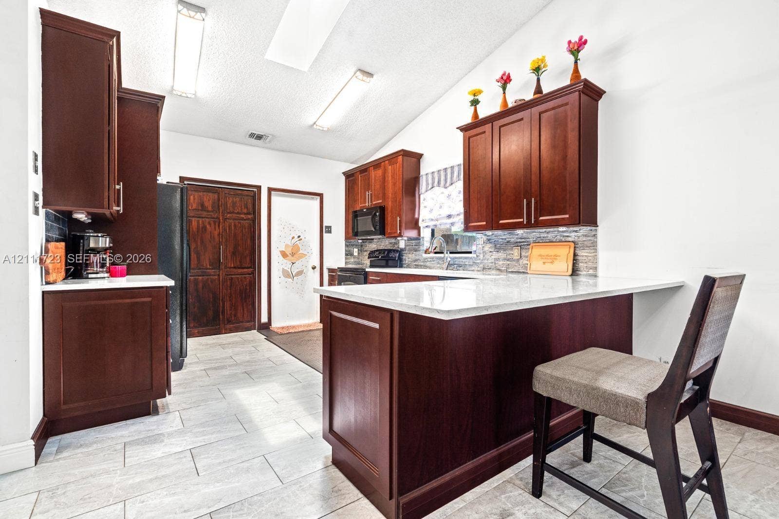 8541 NW 51st Court, Lauderhill, FL 33351 Kitchen featuring dark wood cabinetry, light stone-finish countertops, tile backsplash, tile flooring, and a breakfast bar
