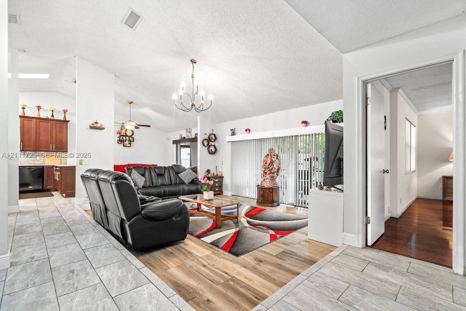 8541 NW 51st Court, Lauderhill, FL 33351 Open-concept living space featuring vaulted ceilings, wood-finish flooring, ceramic tile flooring, a multi-arm chandelier, and sliding glass doors