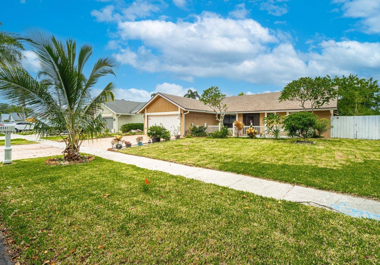 8541 NW 51st Court, Lauderhill, FL 33351 Single-story exterior featuring a shingled roof, attached two-car garage, covered entryway, and mature landscaping