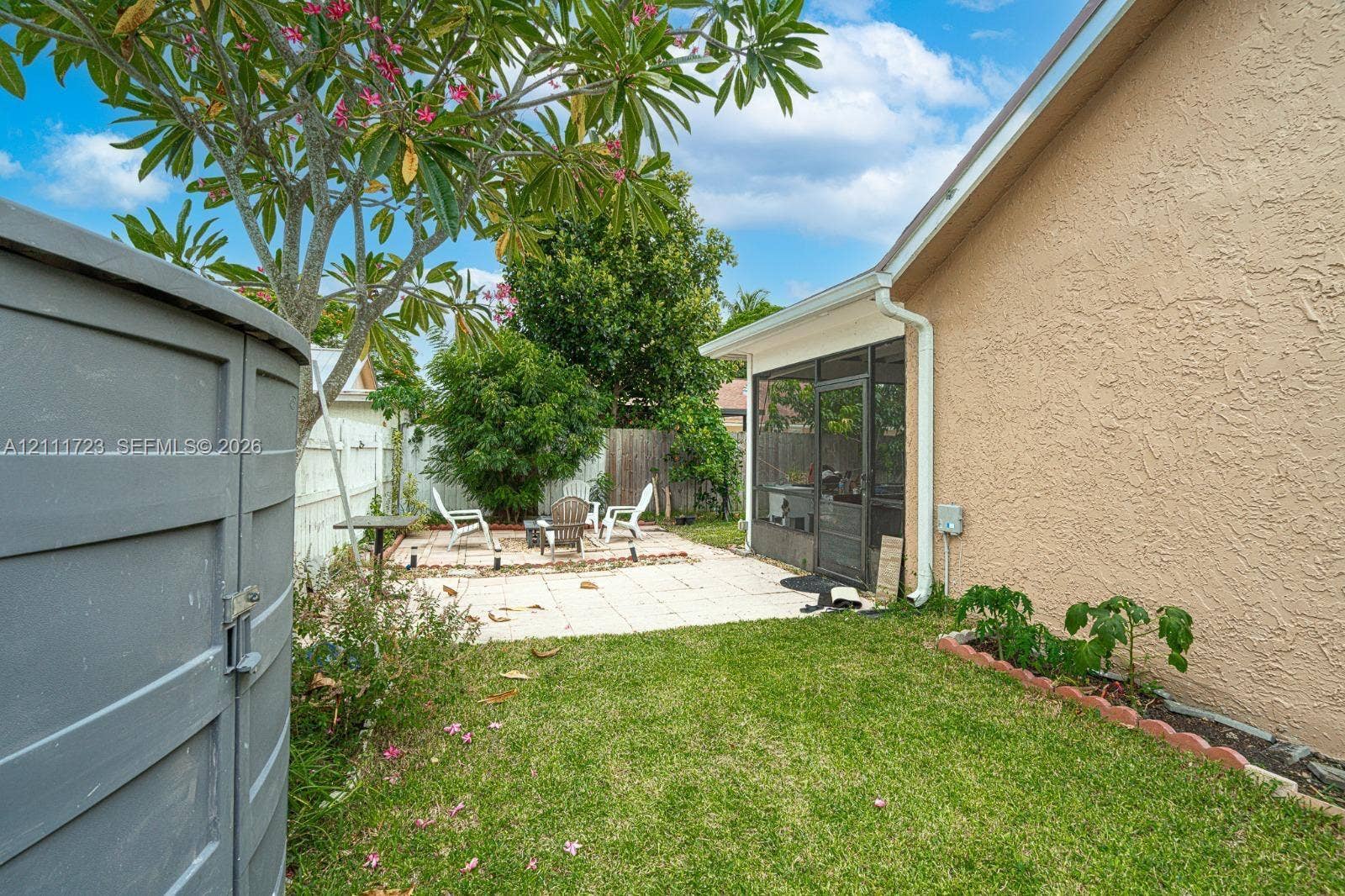 8541 NW 51st Court, Lauderhill, FL 33351 Rear exterior featuring a paved stone patio, screened-in enclosure, stucco siding, and a landscaped lawn with a raised garden border