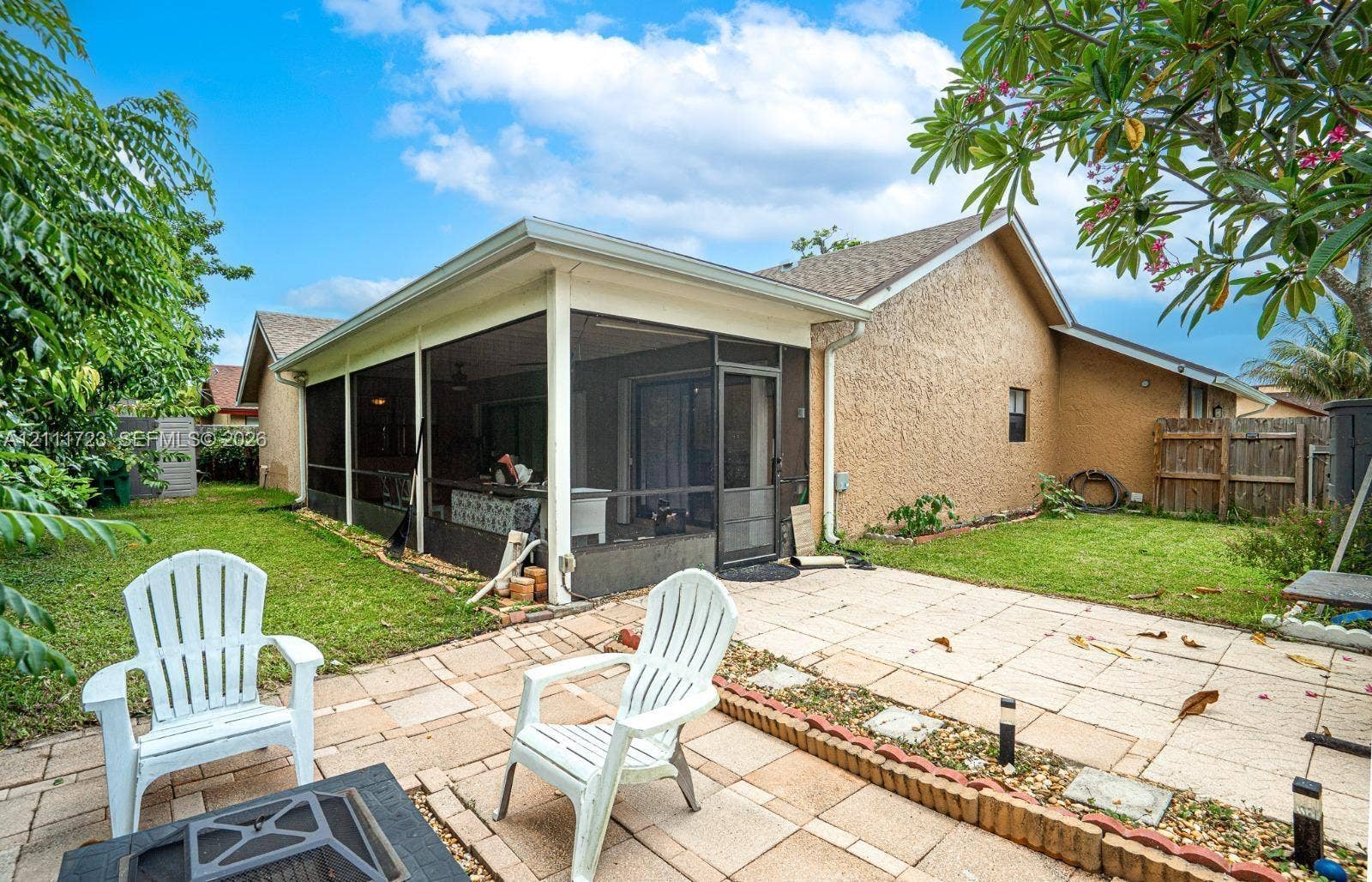 8541 NW 51st Court, Lauderhill, FL 33351 Rear exterior featuring a screened-in patio, concrete paver terrace, and grass lawn with a masonry border