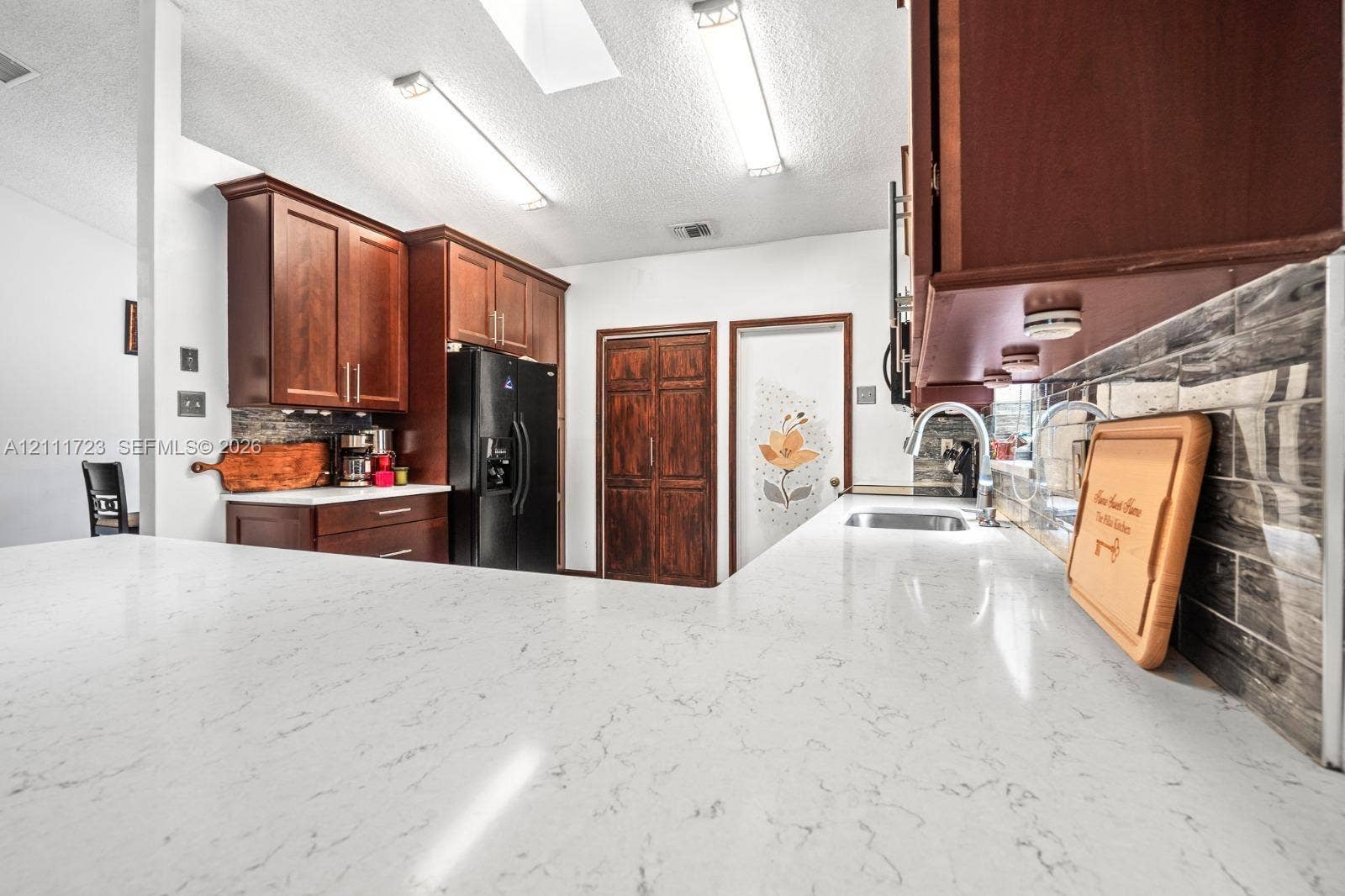 8541 NW 51st Court, Lauderhill, FL 33351 Kitchen featuring stone-finish countertops, dark wood cabinetry, a stainless steel undermount sink with a gooseneck faucet, and a horizontally laid tile backsplash