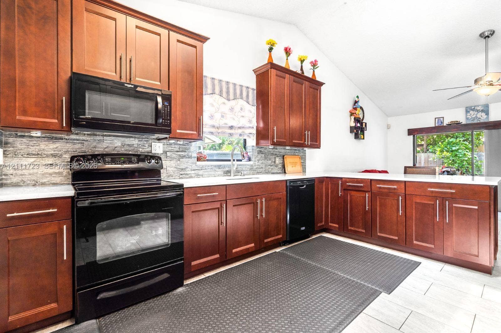 8541 NW 51st Court, Lauderhill, FL 33351 Kitchen featuring wood cabinetry, solid surface countertops, stacked-stone backsplash, black built-in appliances, and vaulted ceilings