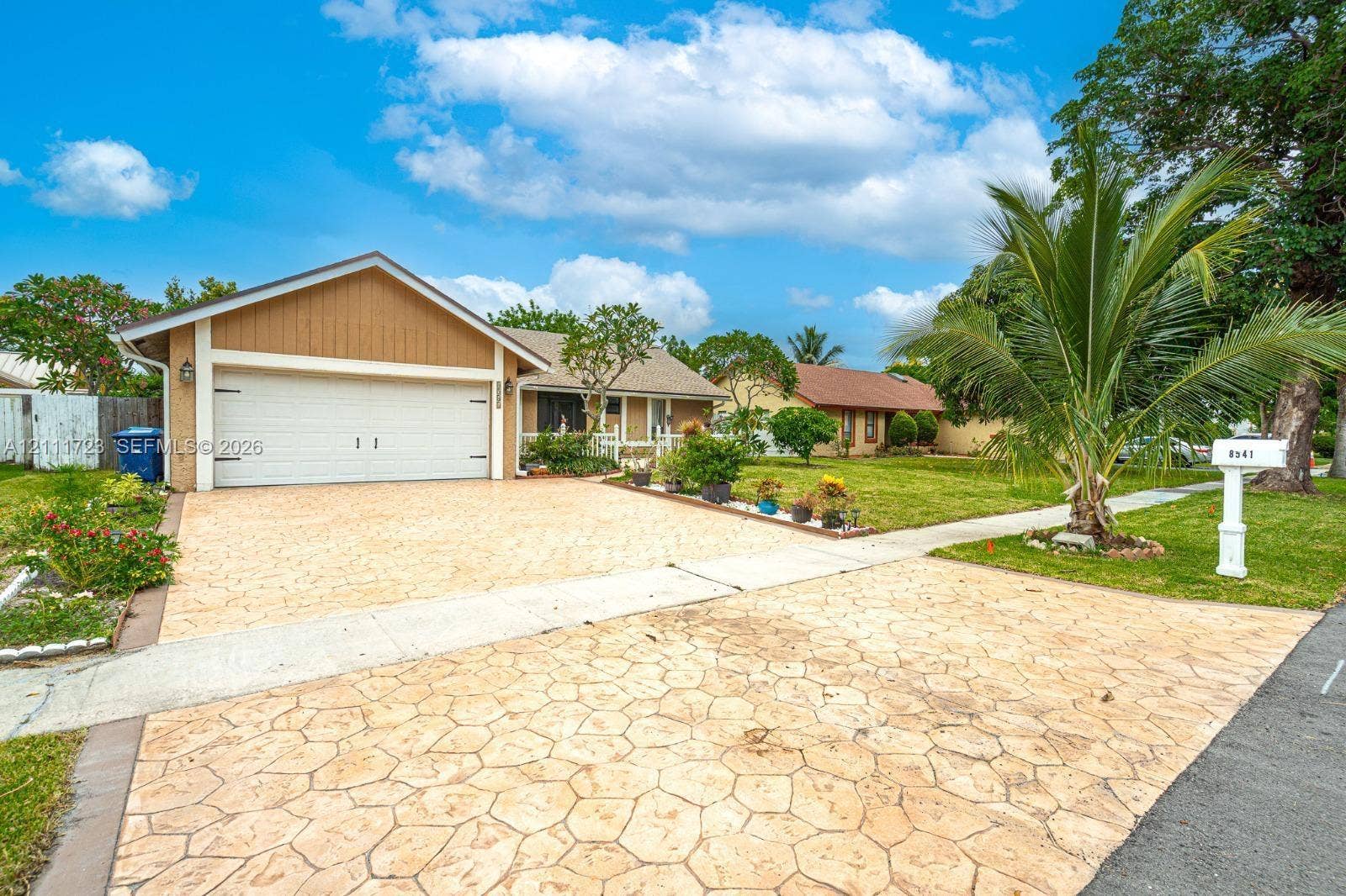 8541 NW 51st Court, Lauderhill, FL 33351 Single-story exterior featuring patterned concrete driveway, two-car garage, and mature landscaping