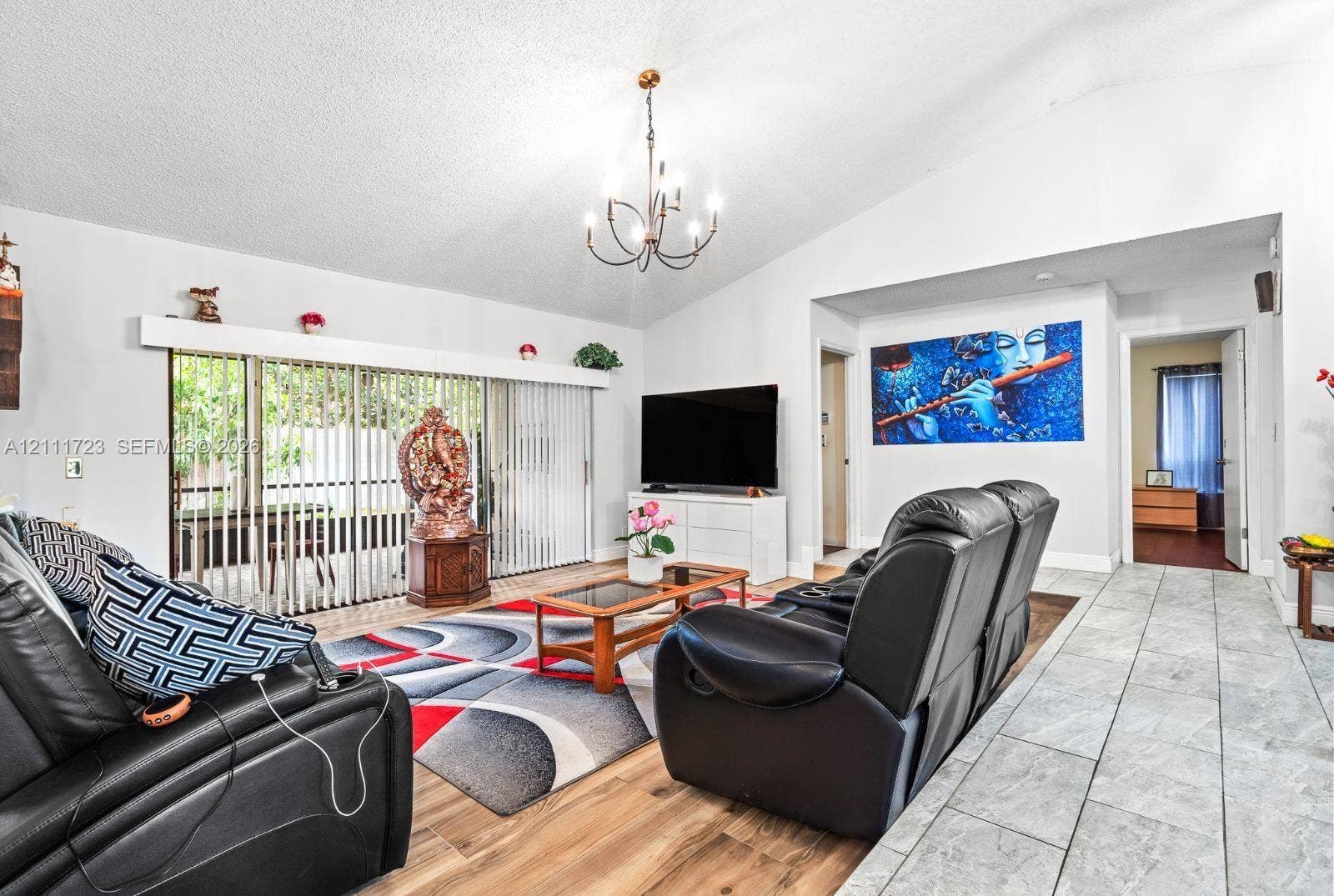 8541 NW 51st Court, Lauderhill, FL 33351 Living area featuring vaulted ceilings, wood-finish flooring, large sliding glass doors, and a multi-arm chandelier