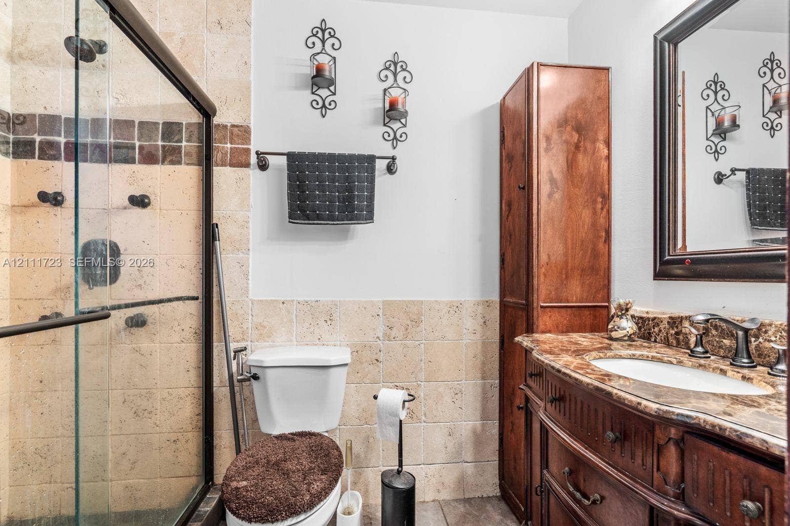8541 NW 51st Court, Lauderhill, FL 33351 Bathroom featuring a glass-enclosed shower with tiled walls, built-in wooden cabinetry, stone-finish vanity countertop with an integrated basin, and a framed wall mirror