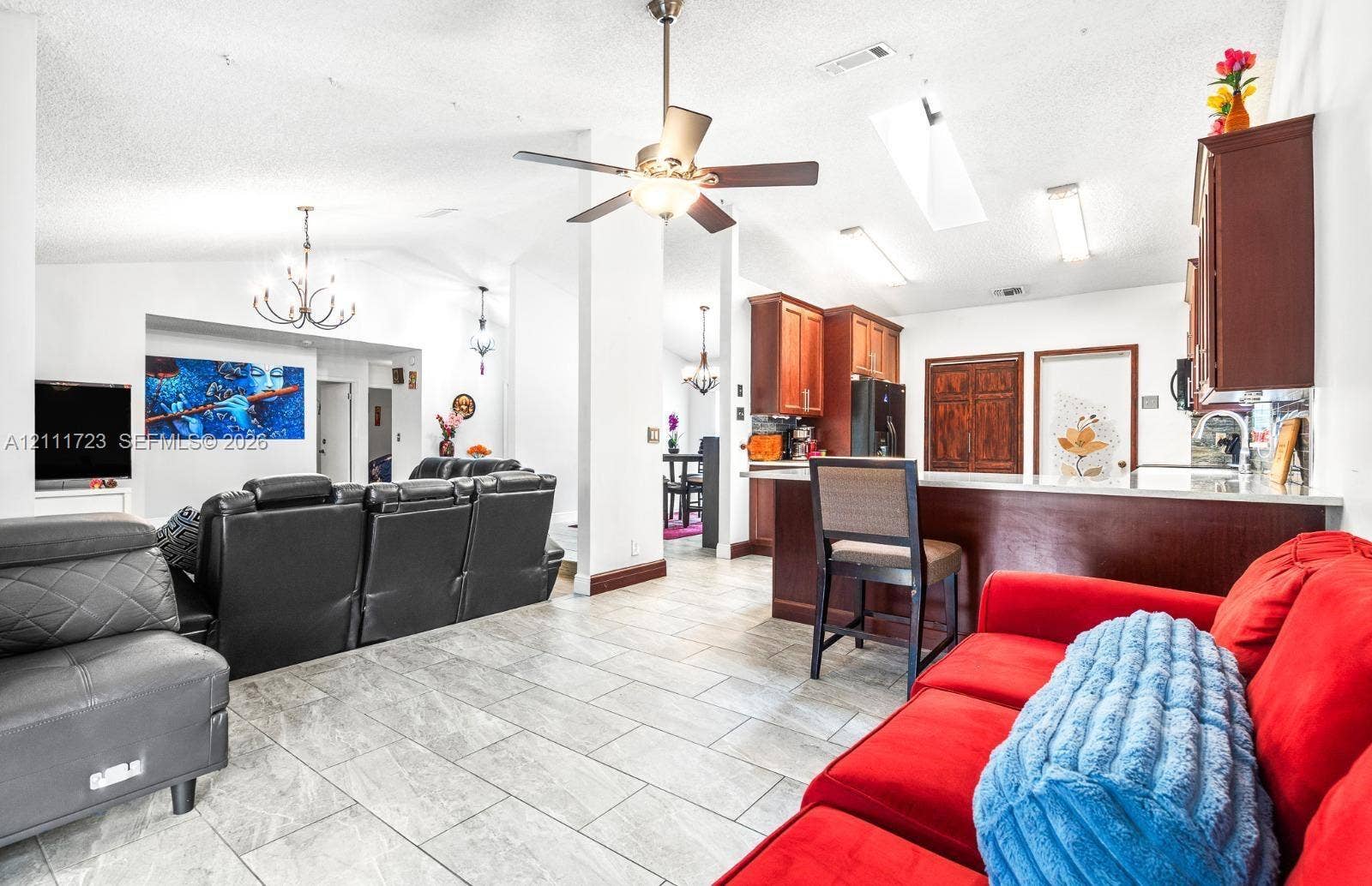 8541 NW 51st Court, Lauderhill, FL 33351 Open-concept interior featuring vaulted ceilings, tile flooring, kitchen cabinetry with a breakfast bar, skylights, and multiple ceiling fans