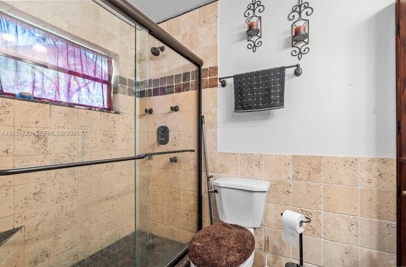 8541 NW 51st Court, Lauderhill, FL 33351 Walk-in shower featuring a frameless glass enclosure, natural stone wall tile with decorative mosaic inlay, and an integrated shower head