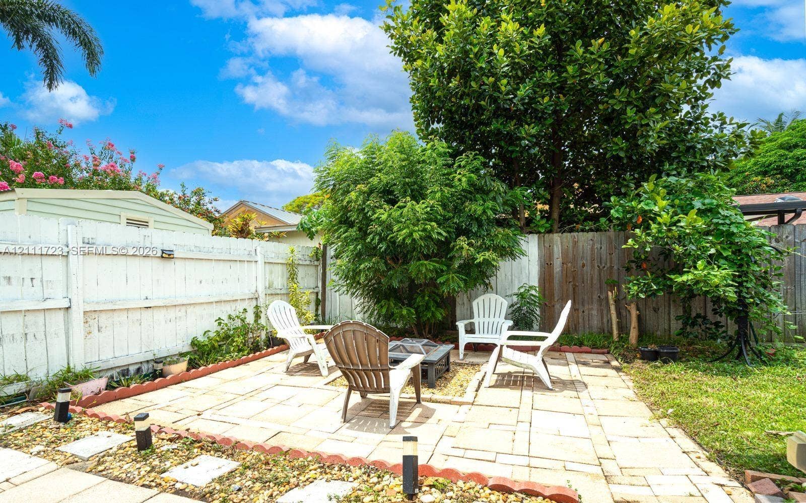 8541 NW 51st Court, Lauderhill, FL 33351 Backyard featuring a paved patio, perimeter wood fencing, mature trees, and garden edging