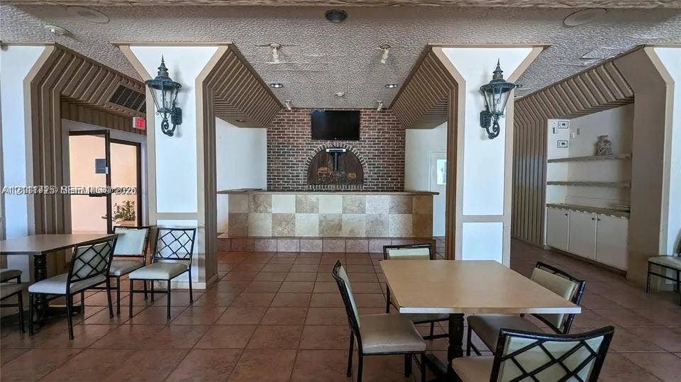 3725 S Ocean Drive, #508, Hollywood, Hollywood, FL 33019 Built-in wet bar featuring a tile-faced counter, brick-accented wall, decorative columns, wall-mounted light fixtures, and integrated cabinetry