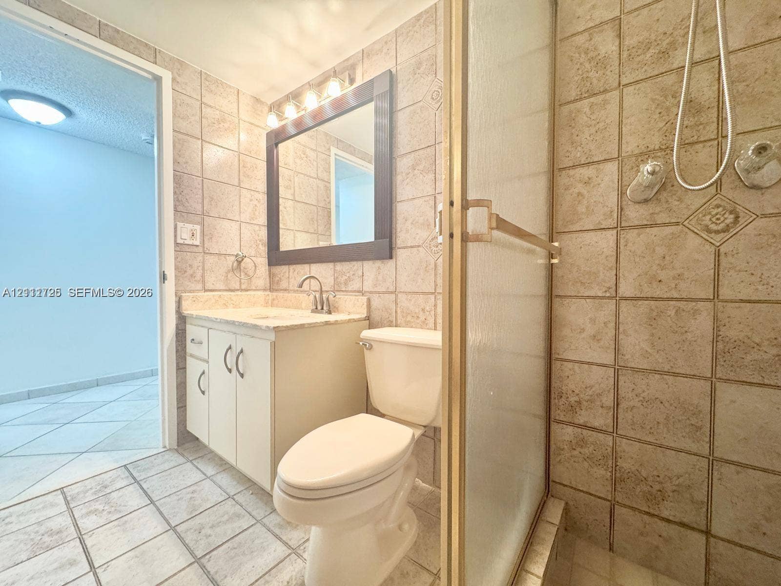 3725 S Ocean Drive, #508, Hollywood, Hollywood, FL 33019 Bathroom featuring a tiled walk-in shower with a gold-tone frame, vanity with neutral-toned countertop, framed wall mirror, and integrated lighting