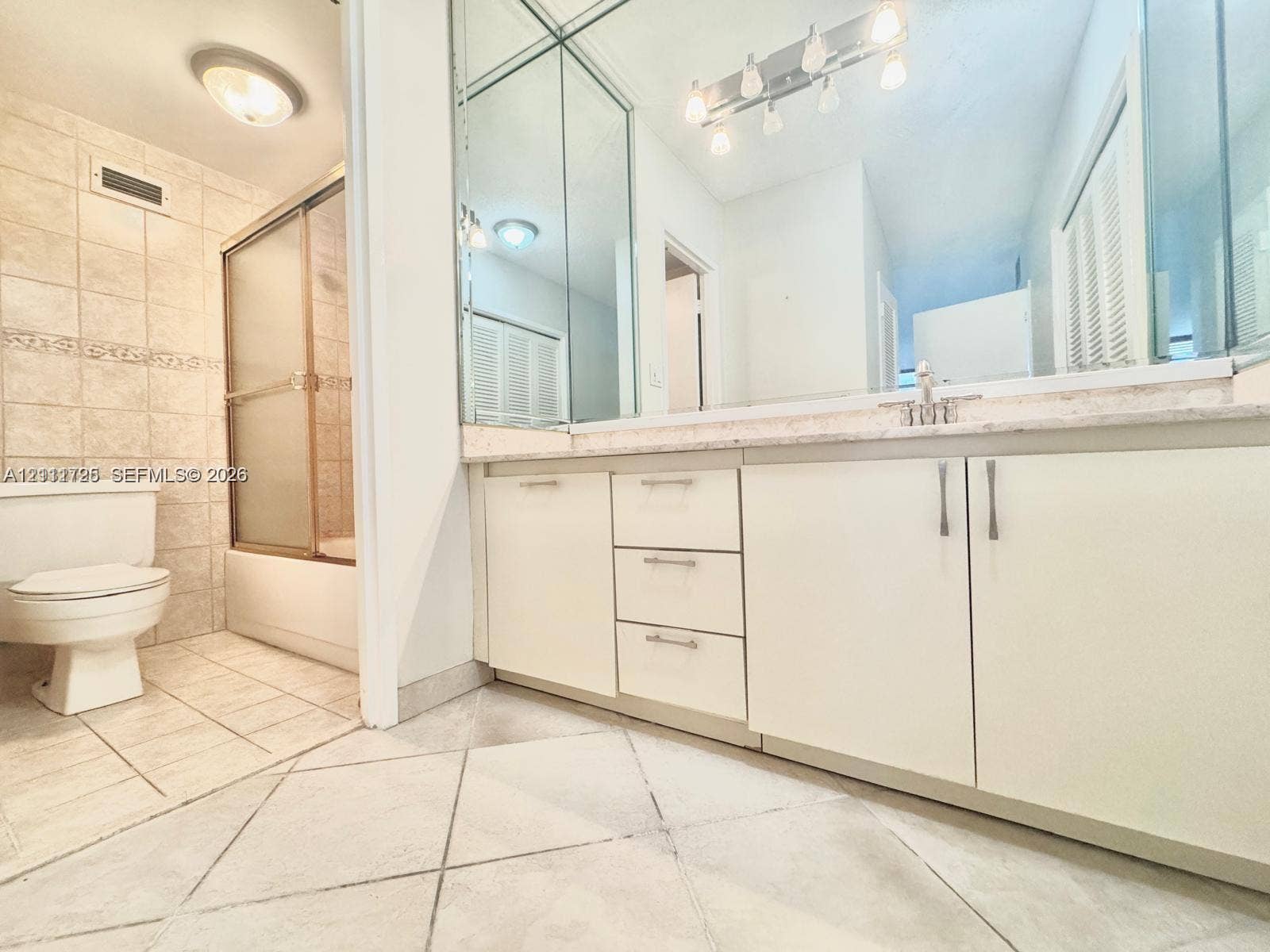 3725 S Ocean Drive, #508, Hollywood, Hollywood, FL 33019 Bathroom featuring a vanity with slab countertop, large-format tiled flooring, full-wall mirror, shower enclosure with tiled surround, and cabinetry with metal hardware