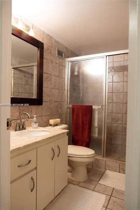 3725 S Ocean Drive, #508, Hollywood, Hollywood, FL 33019 Bathroom featuring a vanity with a neutral countertop and integrated sink, a framed mirror, a walk-in shower with a glass door, and stone-finish wall and floor tile