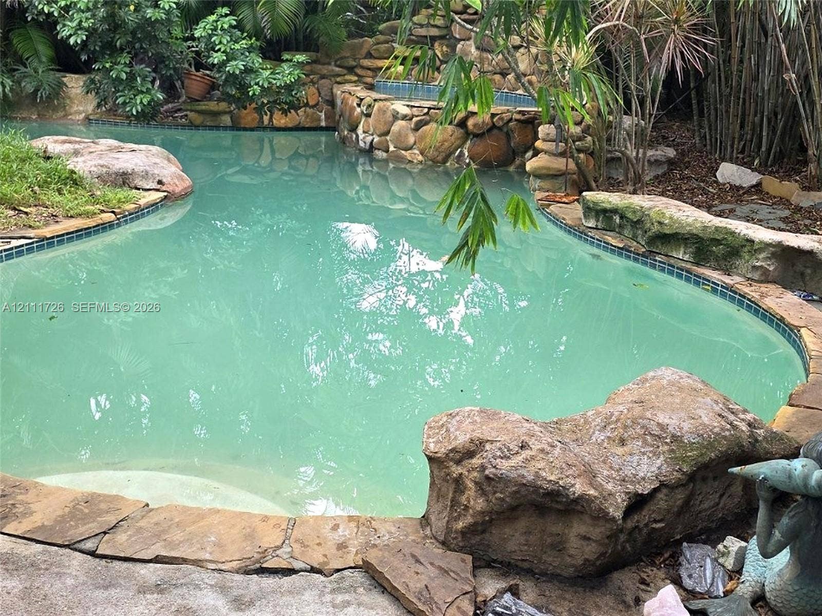 2399 NE 5th Avenue, Boca Raton, FL 33431 Freeform swimming pool featuring a natural stone border, integrated stone waterfall, built-in tiled spa, and large decorative boulders