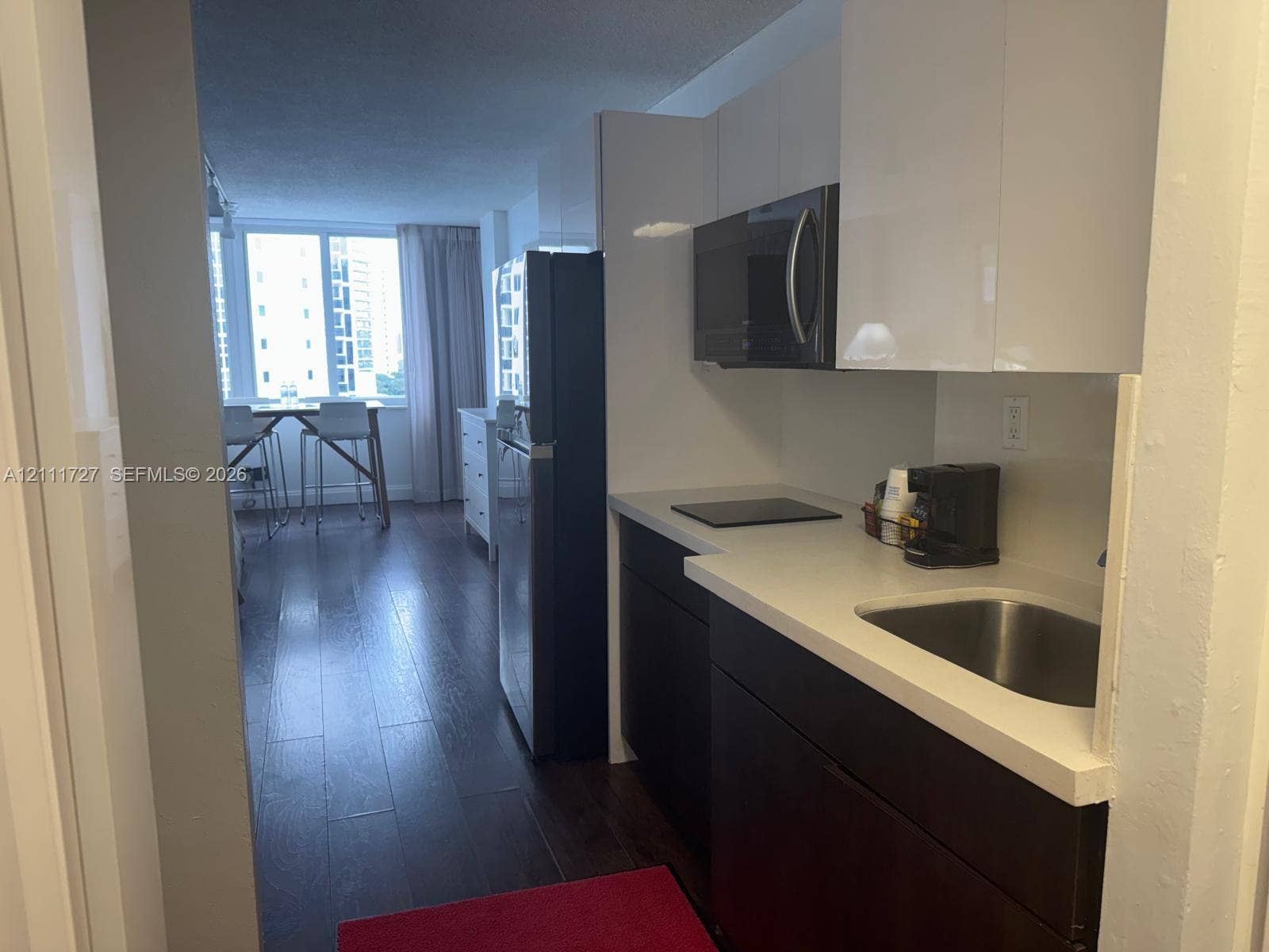 19201 Collins Avenue, #704, Sunny Isles Beach, FL 33160 Kitchen featuring high-gloss white upper cabinetry, dark lower cabinetry, stone-finish countertops, stainless steel sink, and wood-finish flooring
