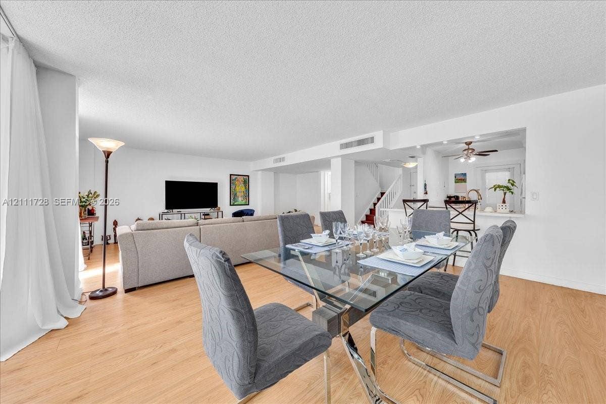 Open-concept interior featuring light wood-finish flooring, a pass-through kitchen window, and a built-in staircase